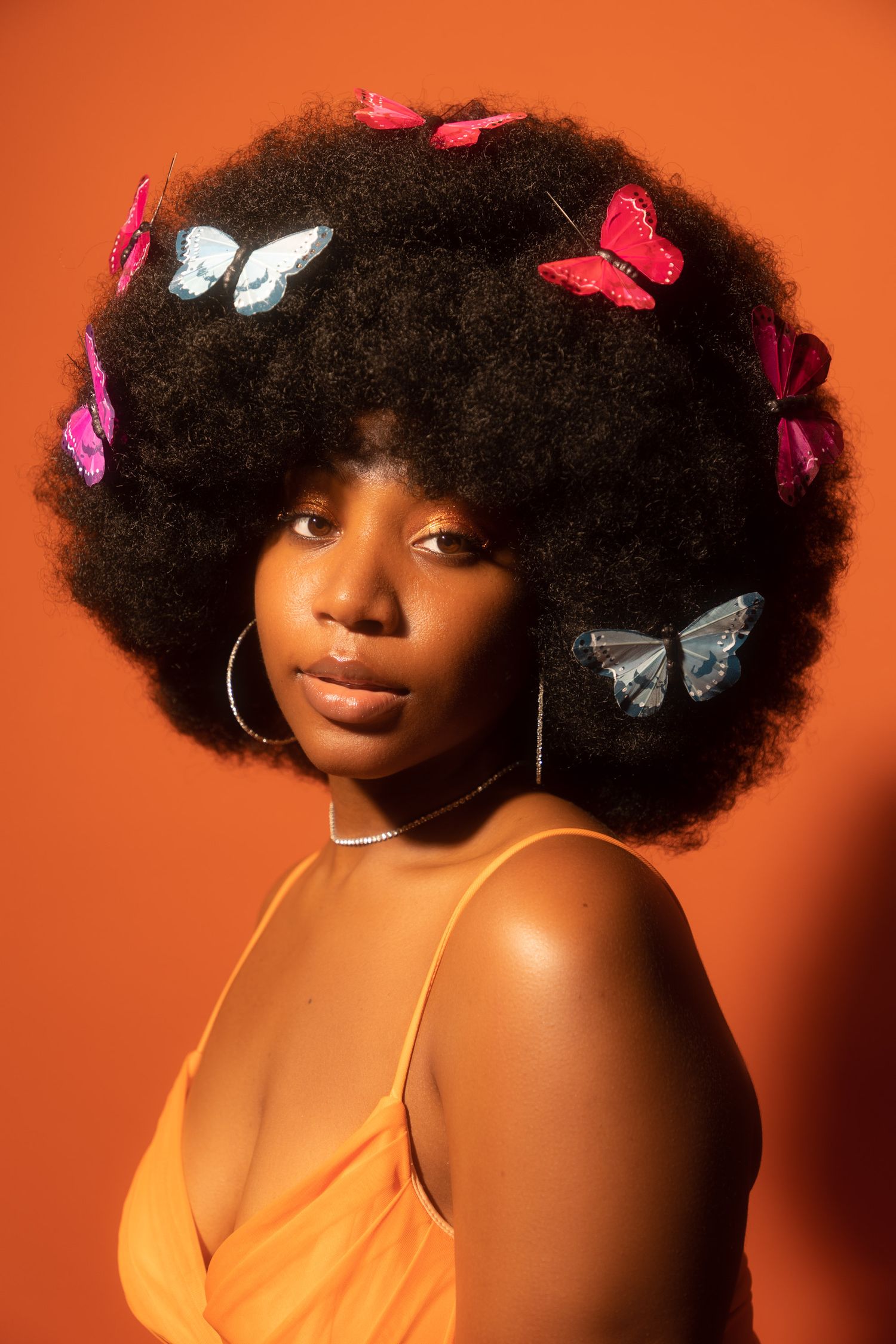 Artistic portrait with butterflies against orange background with dramatic lighting.