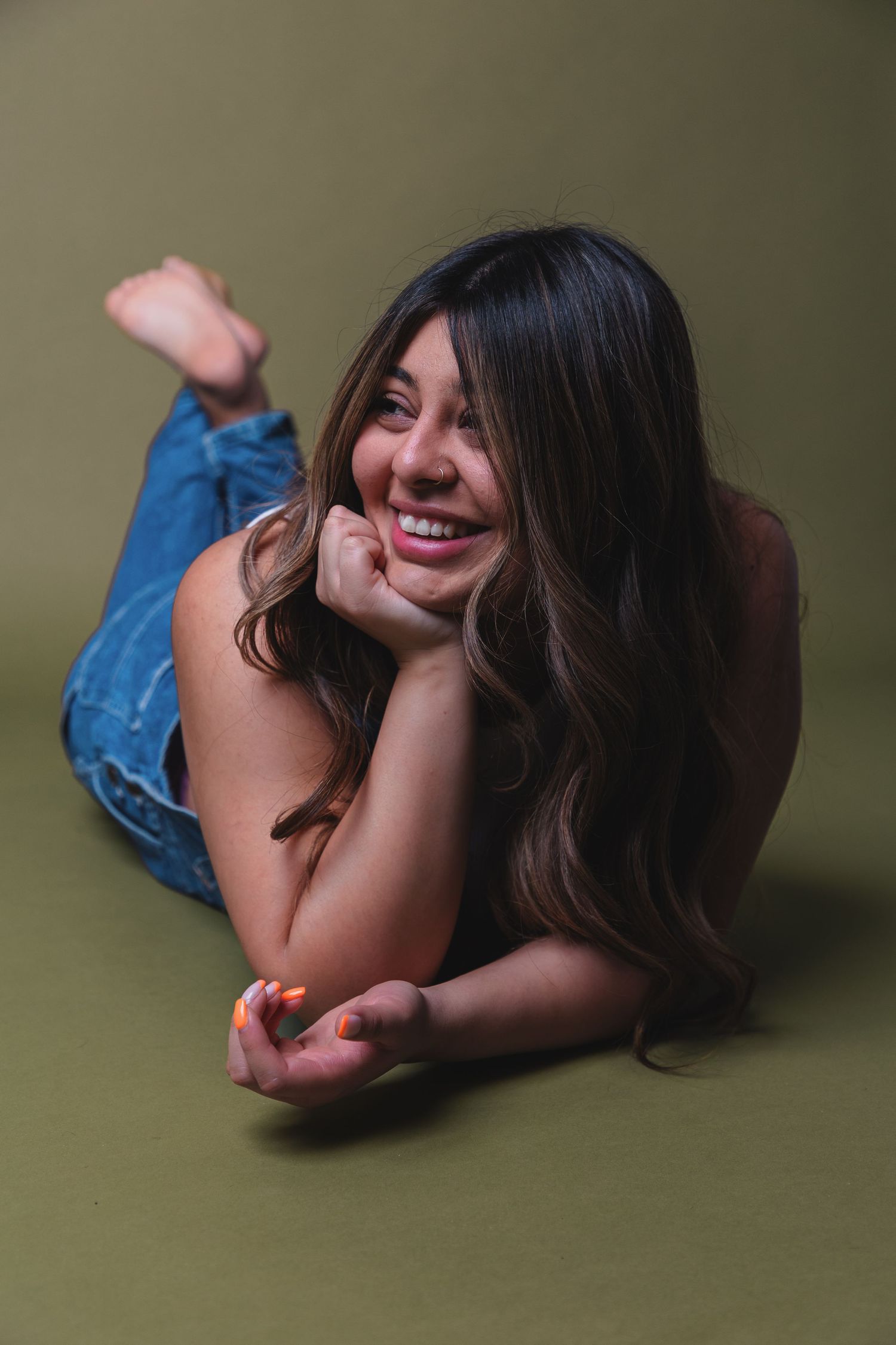 A person in denim lies on a green backdrop during a casual photo session.