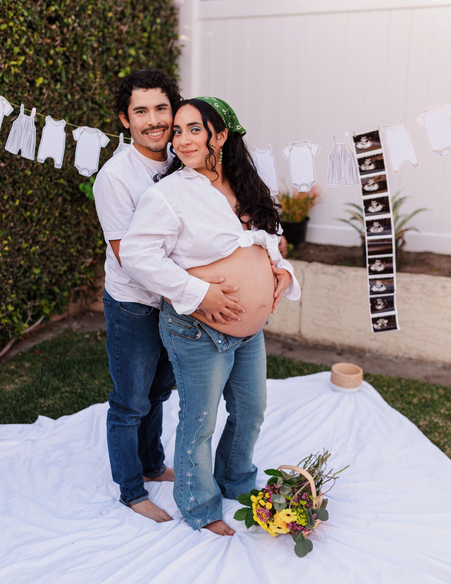Pregnancy announcement photos on white blanket with ultrasound images and sunflowers.