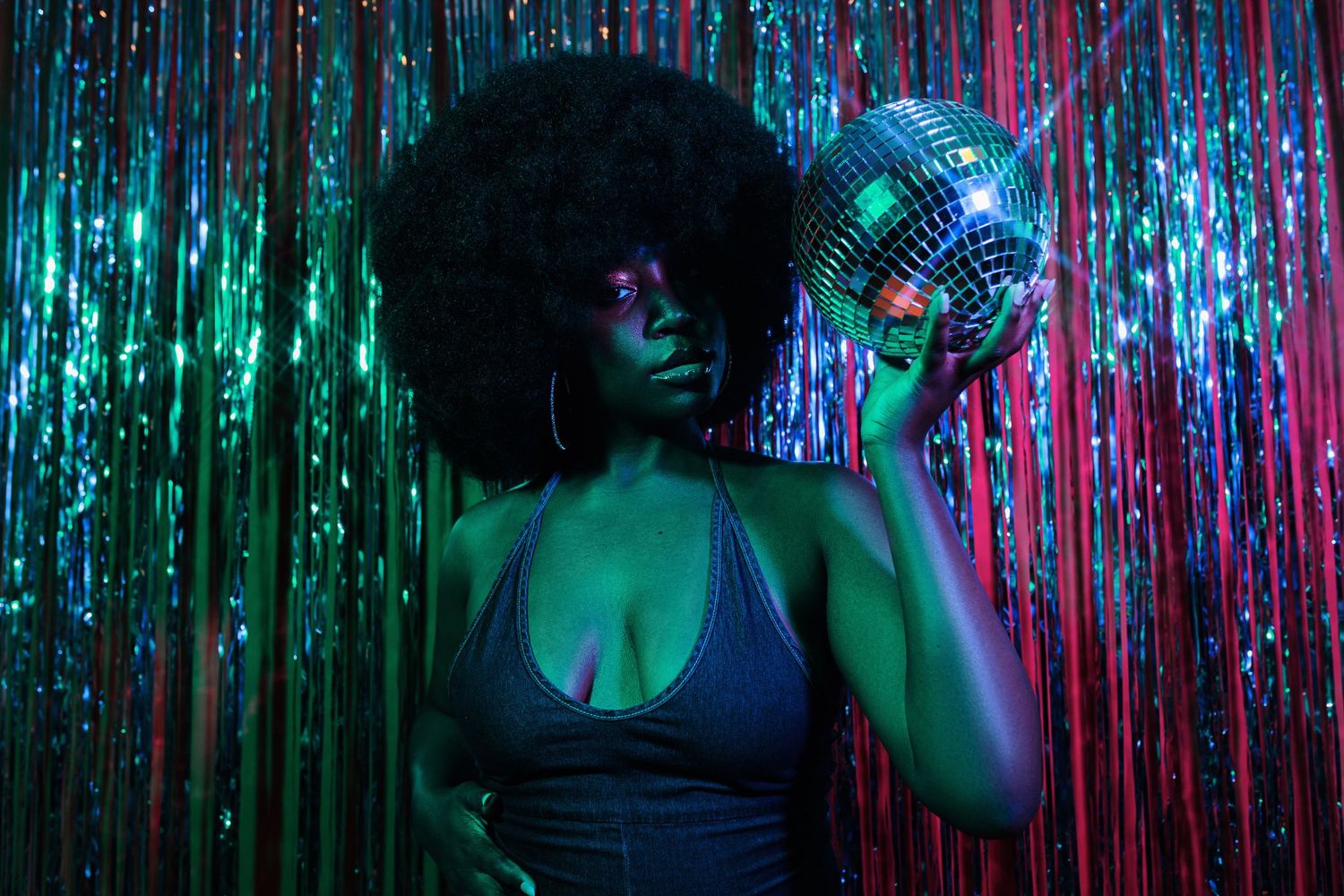 Dramatic portrait with disco ball against sparkly backdrop in moody blue lighting.