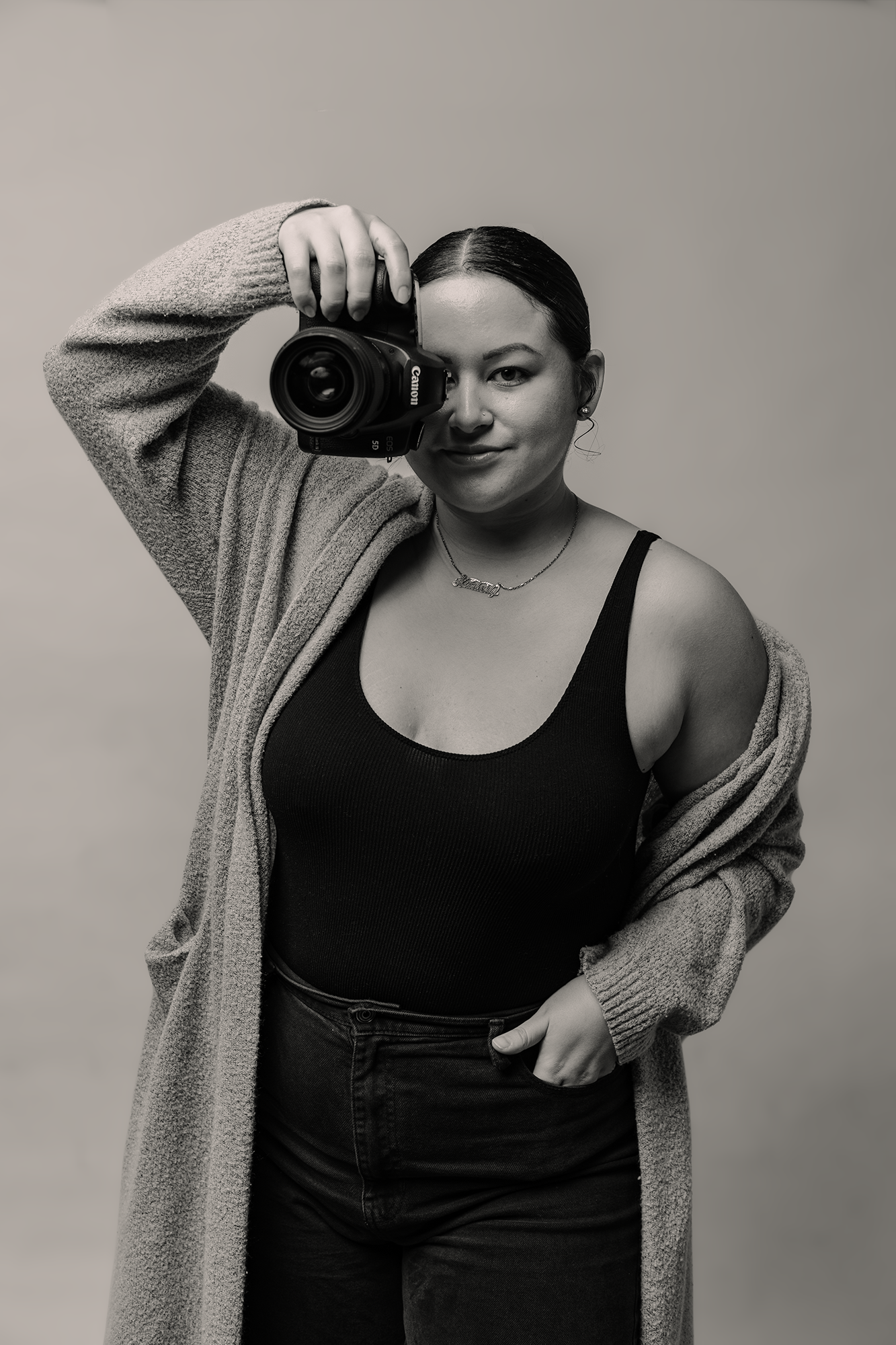 Portrait of photographer holding professional camera wearing gray cardigan against neutral background.