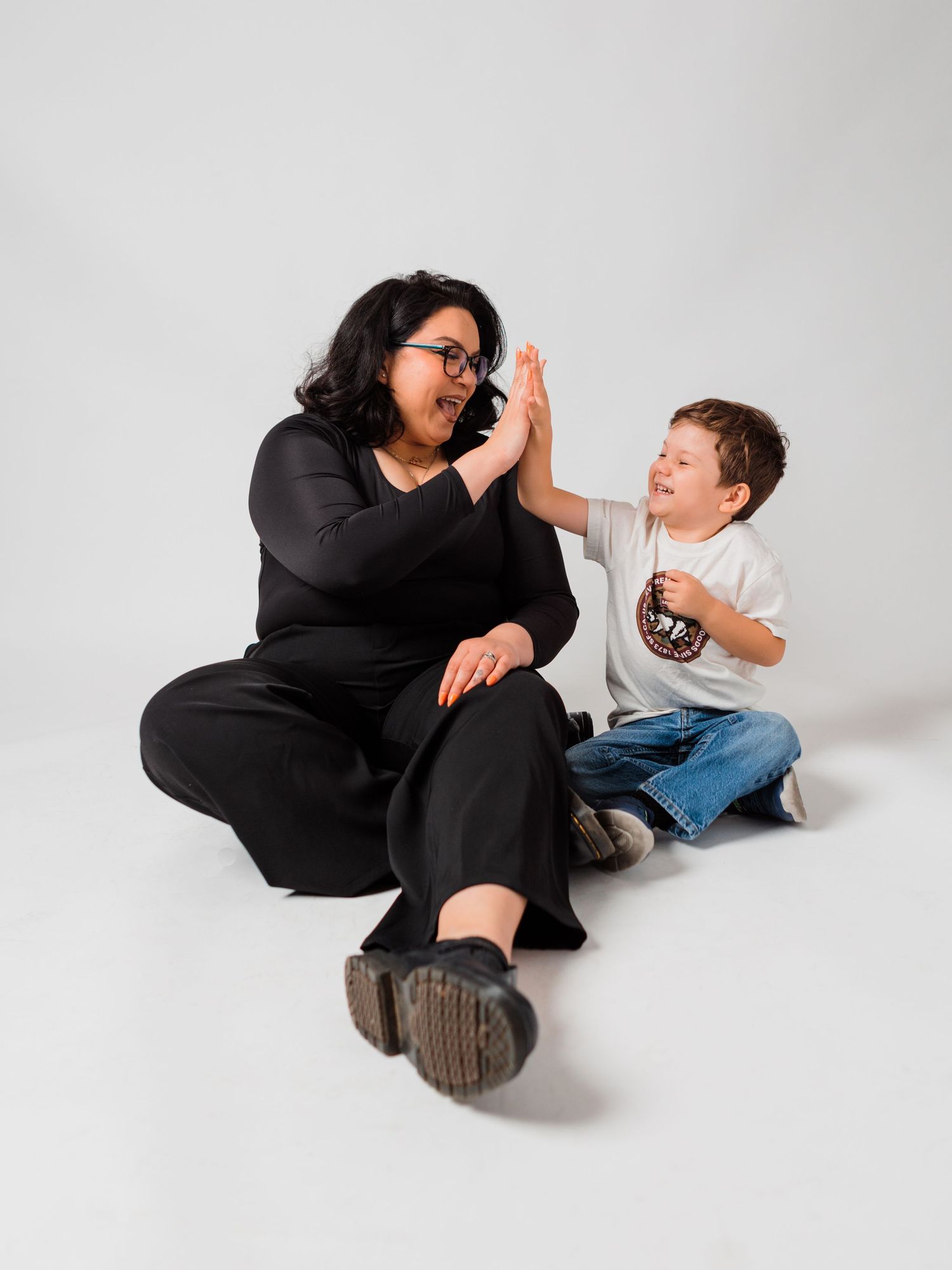A joyful moment captured as two people share a high-five while sitting on a white studio floor.