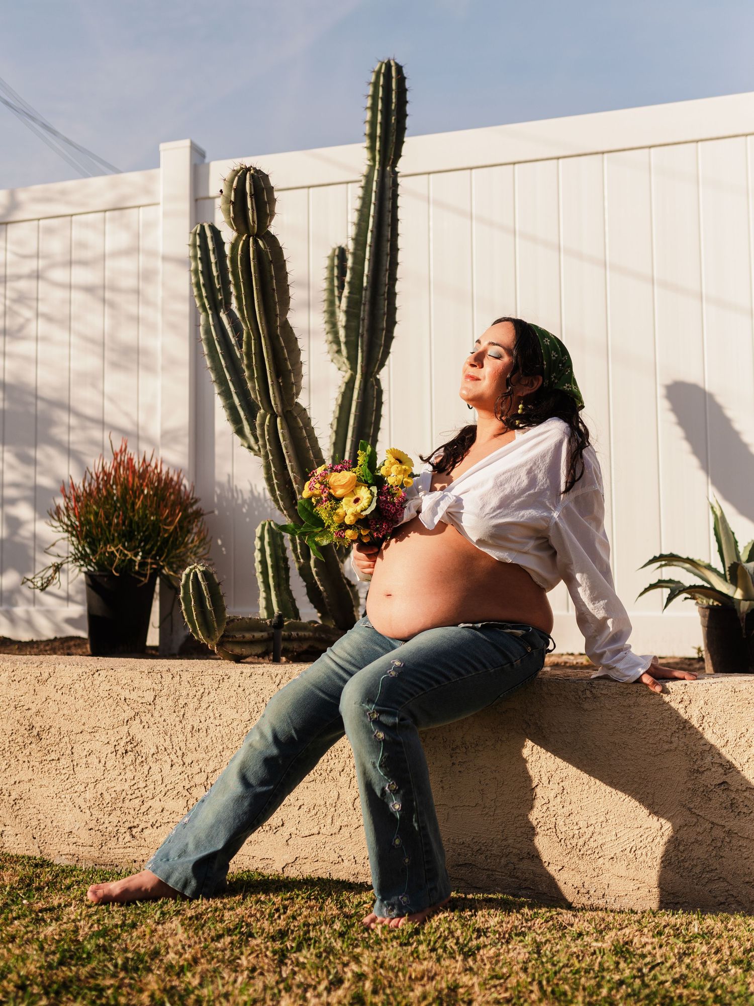 Maternity photoshoot in a garden setting with cacti and white fence.