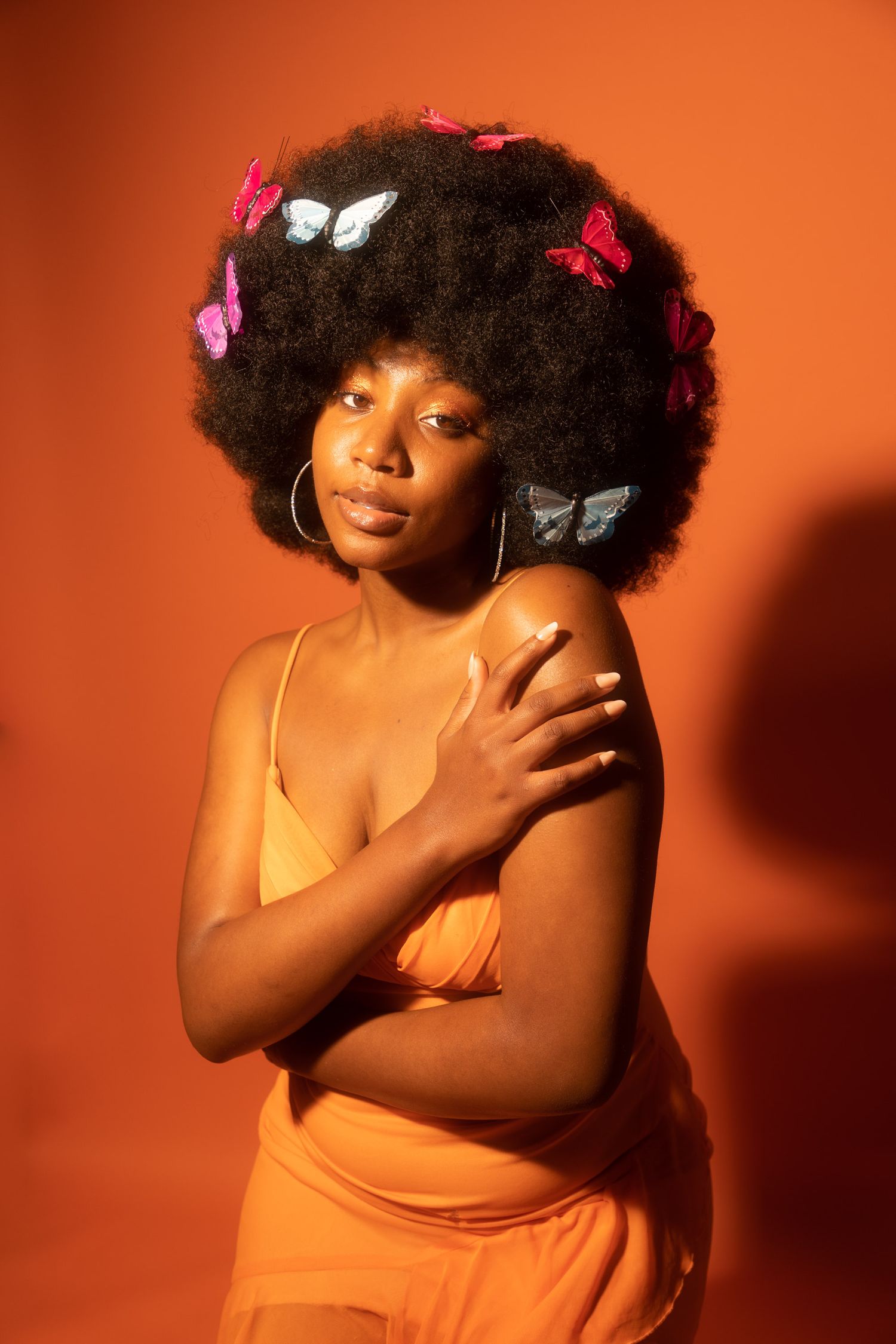 Elegant pose with butterfly accessories against warm orange backdrop.
