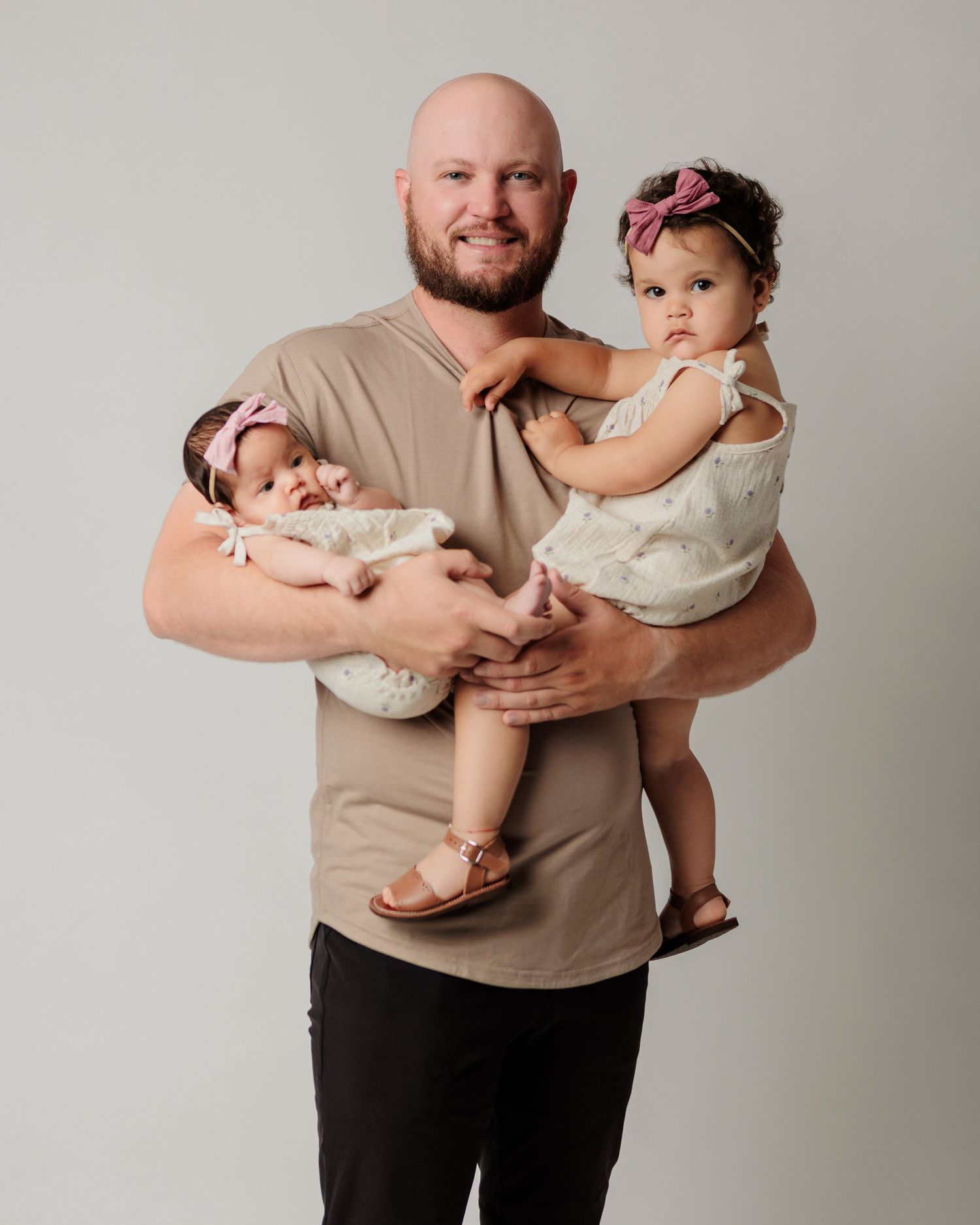 A parent holds two small children against a neutral grey studio background.