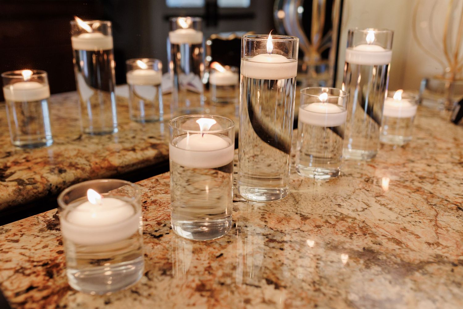 Floating candles in glass cylinders with water on a granite countertop, creating elegant ambient lighting.