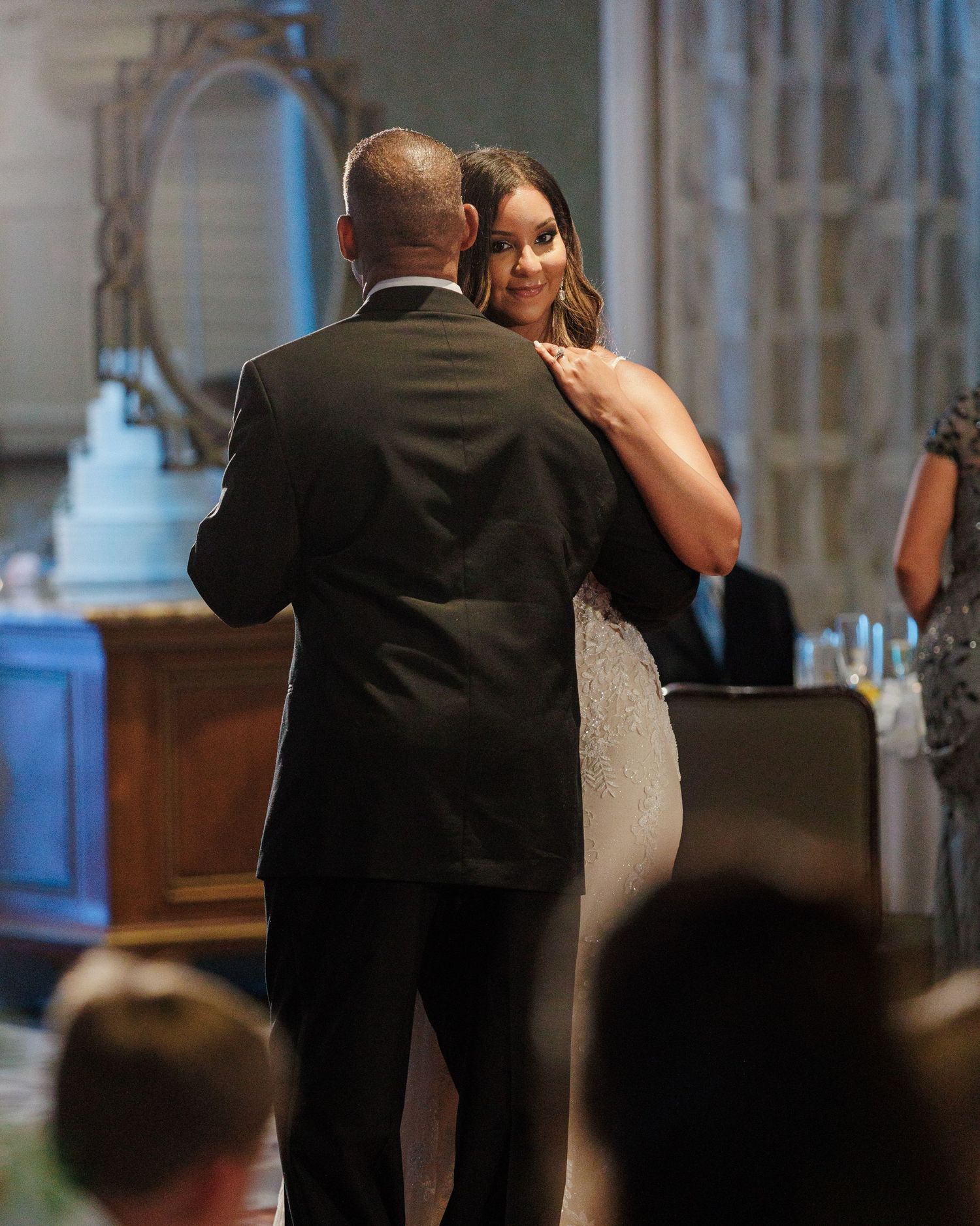 Bride and groom sharing their first dance at wedding reception with blue cake visible in background.