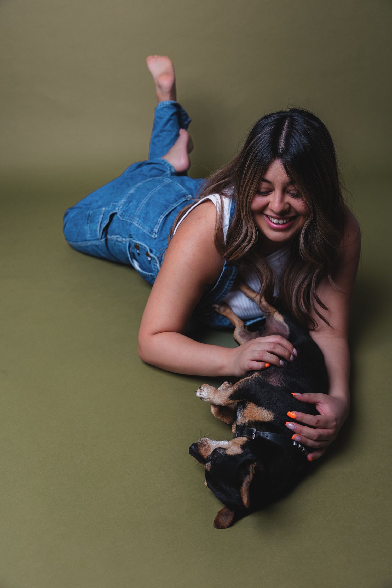 A person in denim plays with a small dog on a green studio backdrop.