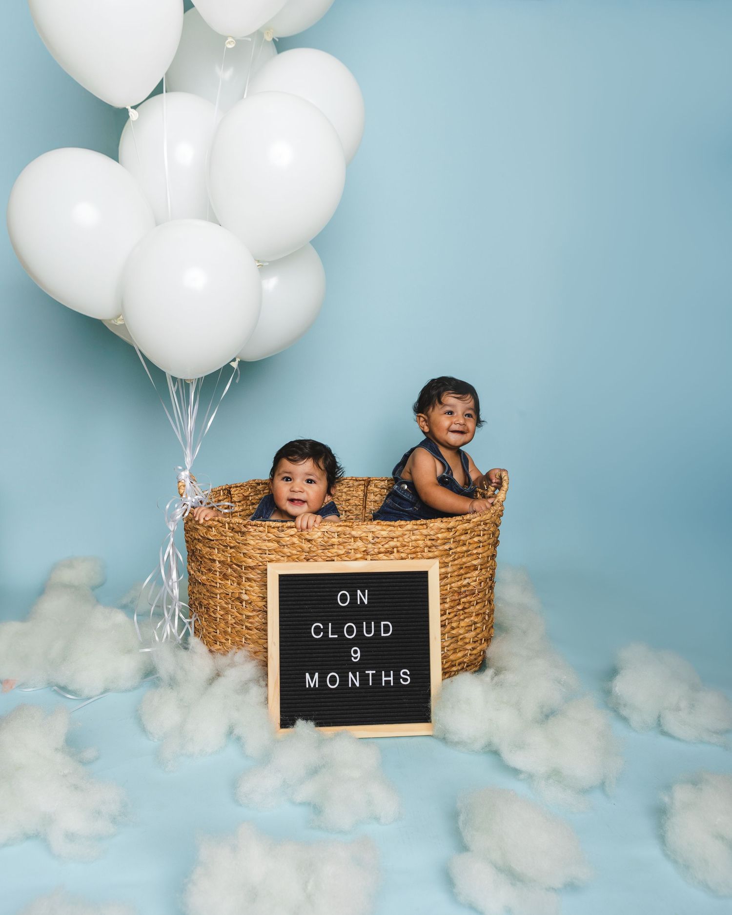 Baby milestone photo with white balloons and letter board reading 'On Cloud 9 Months' against blue background.