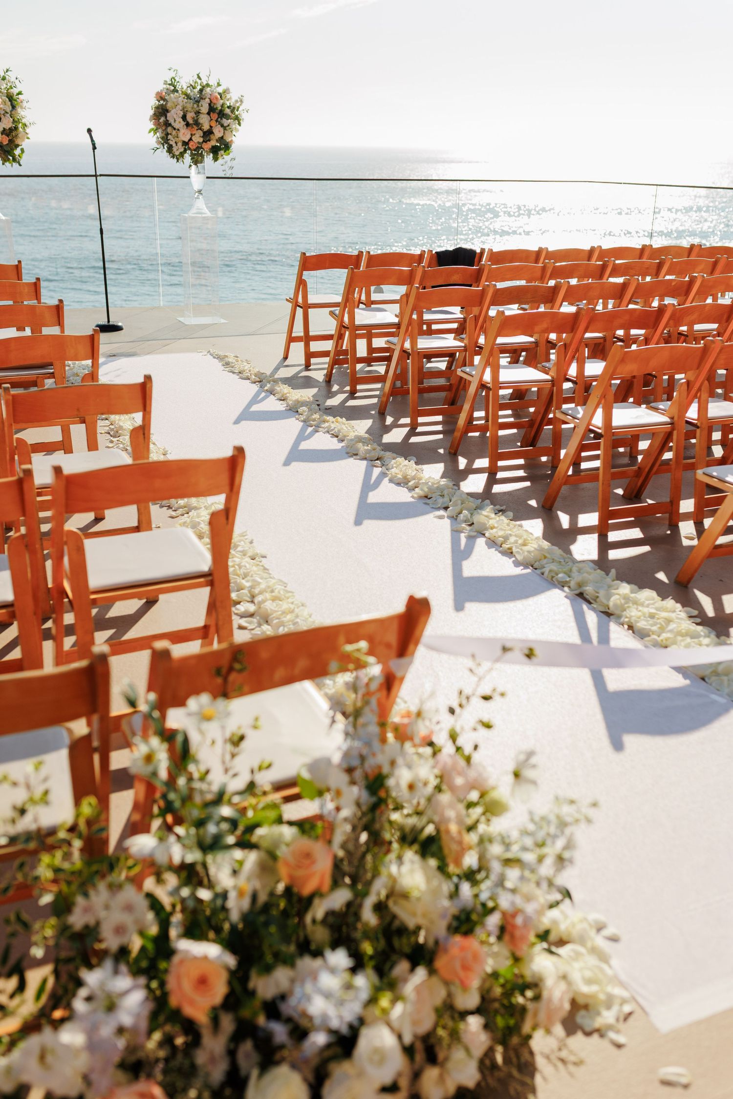 Orange County wedding ceremony setup with orange folding chairs, floral arrangements, and ocean views.
