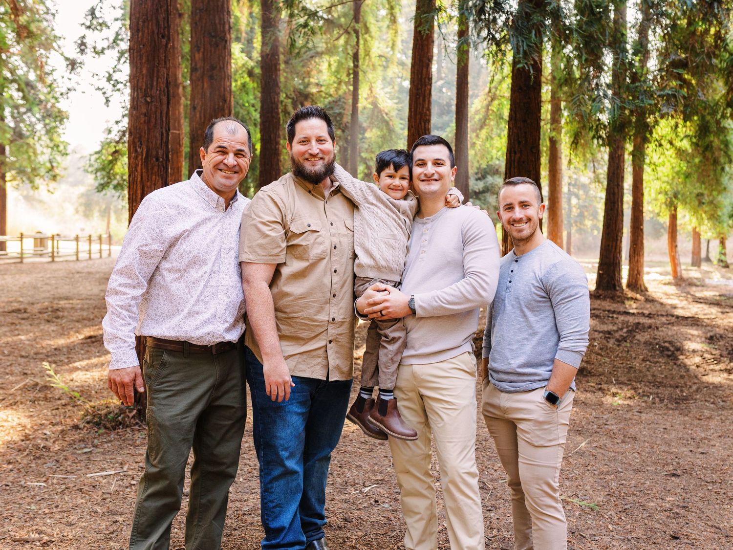 A group of friends in casual attire pose together on a forest path.