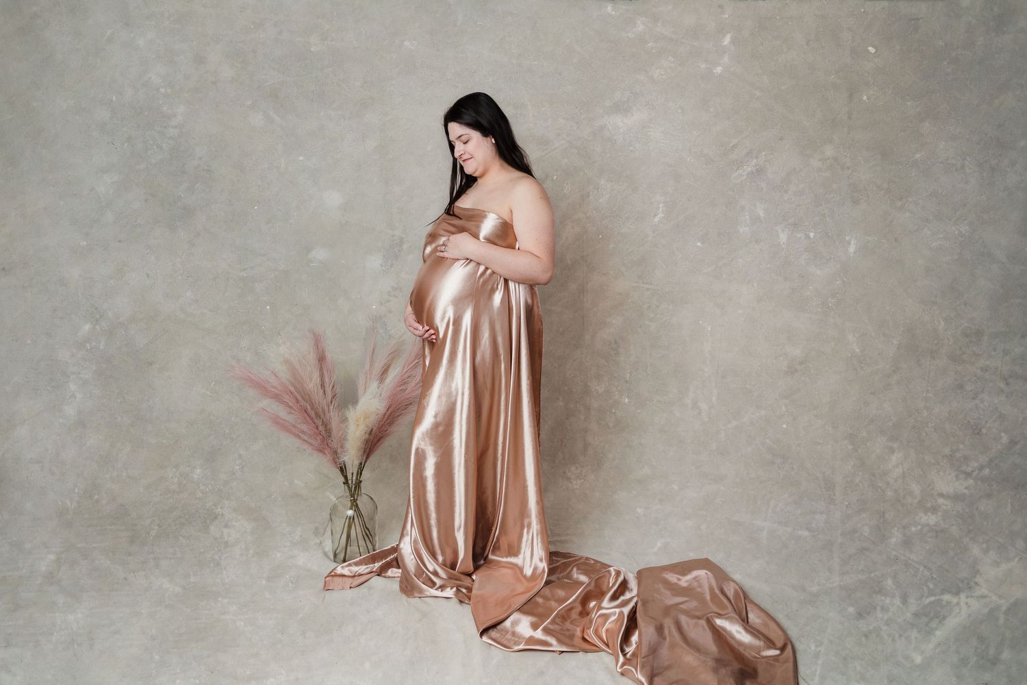 Elegant maternity photography series in rose gold dress against textured grey wall.