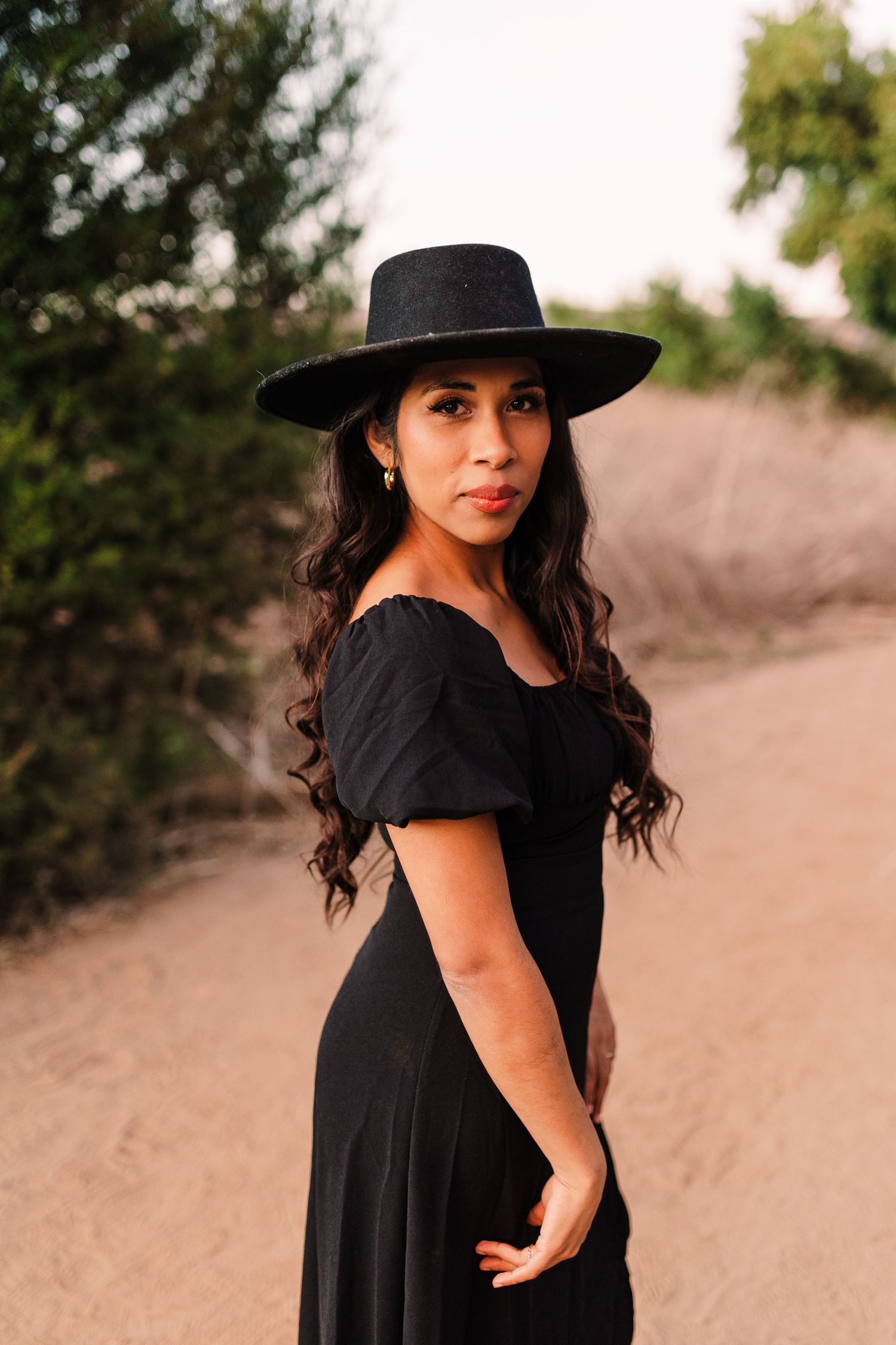 Outdoor fashion photos in black dress and hat against desert landscape at sunset.