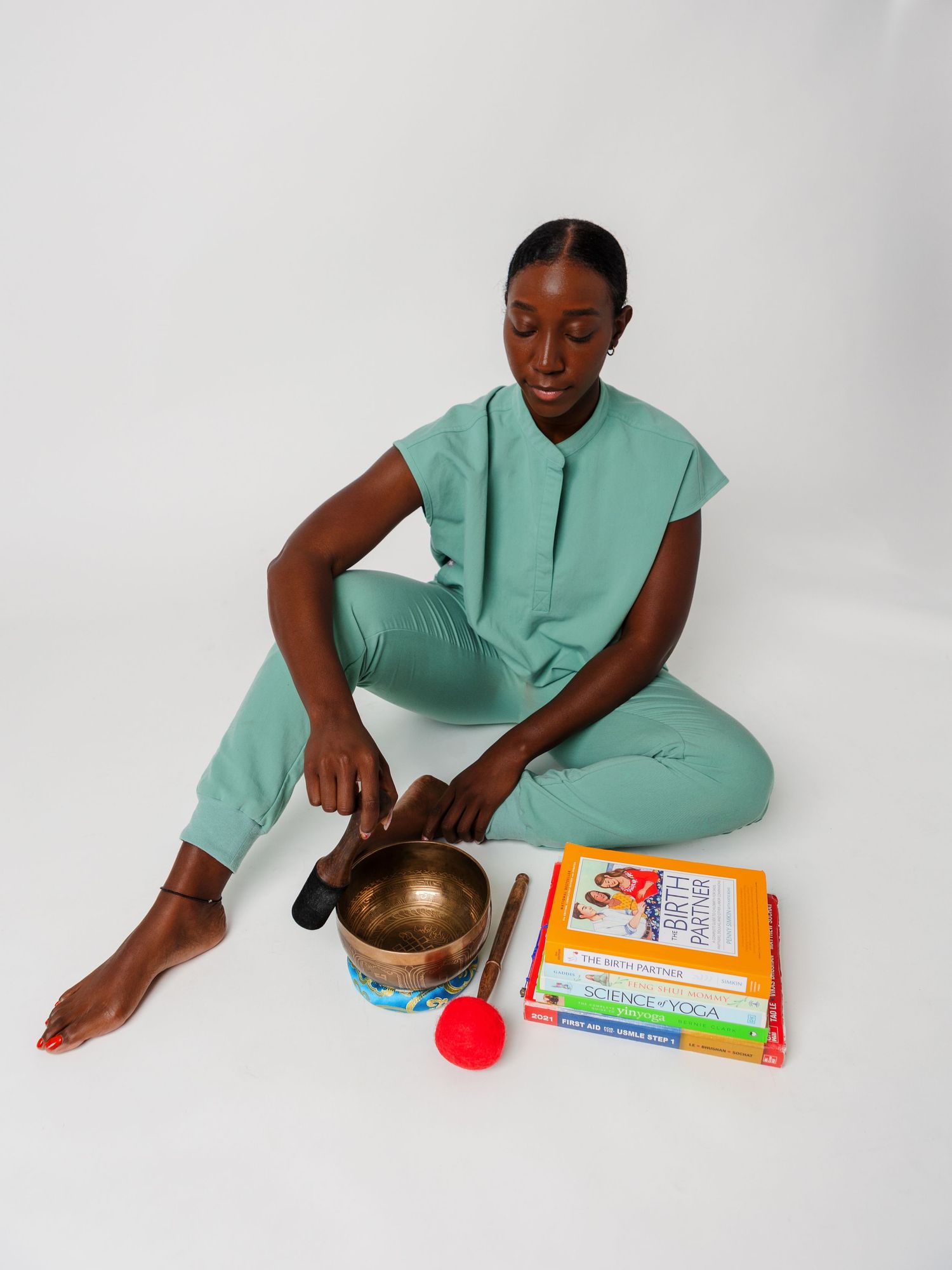 Person in mint green outfit with meditation bowl and books on white background.