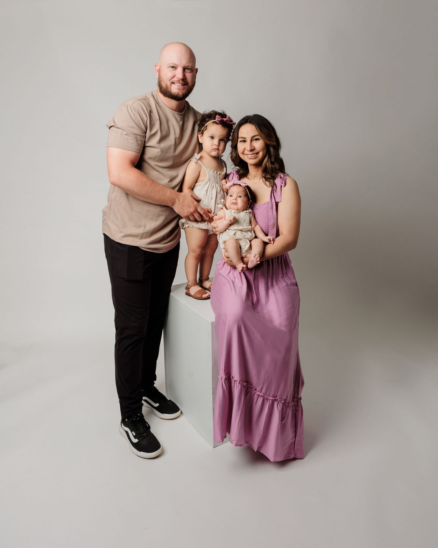 A family portrait against a grey backdrop with coordinated neutral-toned outfits.