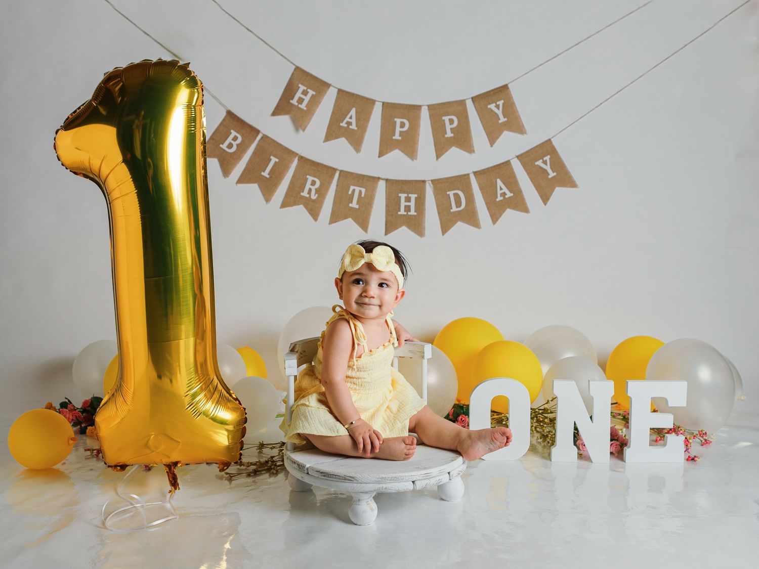 First birthday setup with gold balloon, ONE letters, and decorations in white and yellow.