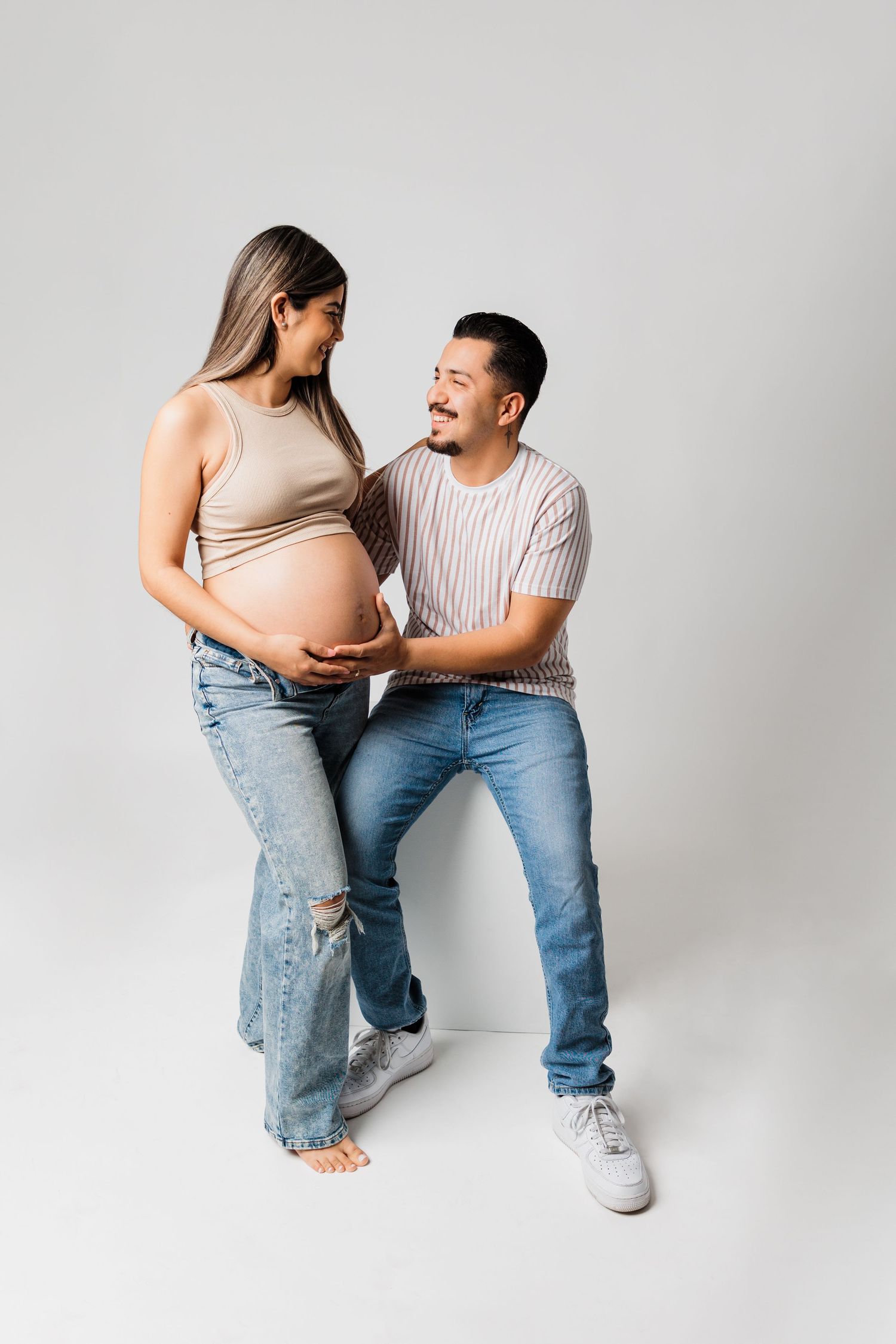 Joyful maternity photo with couple in casual wear against white background.