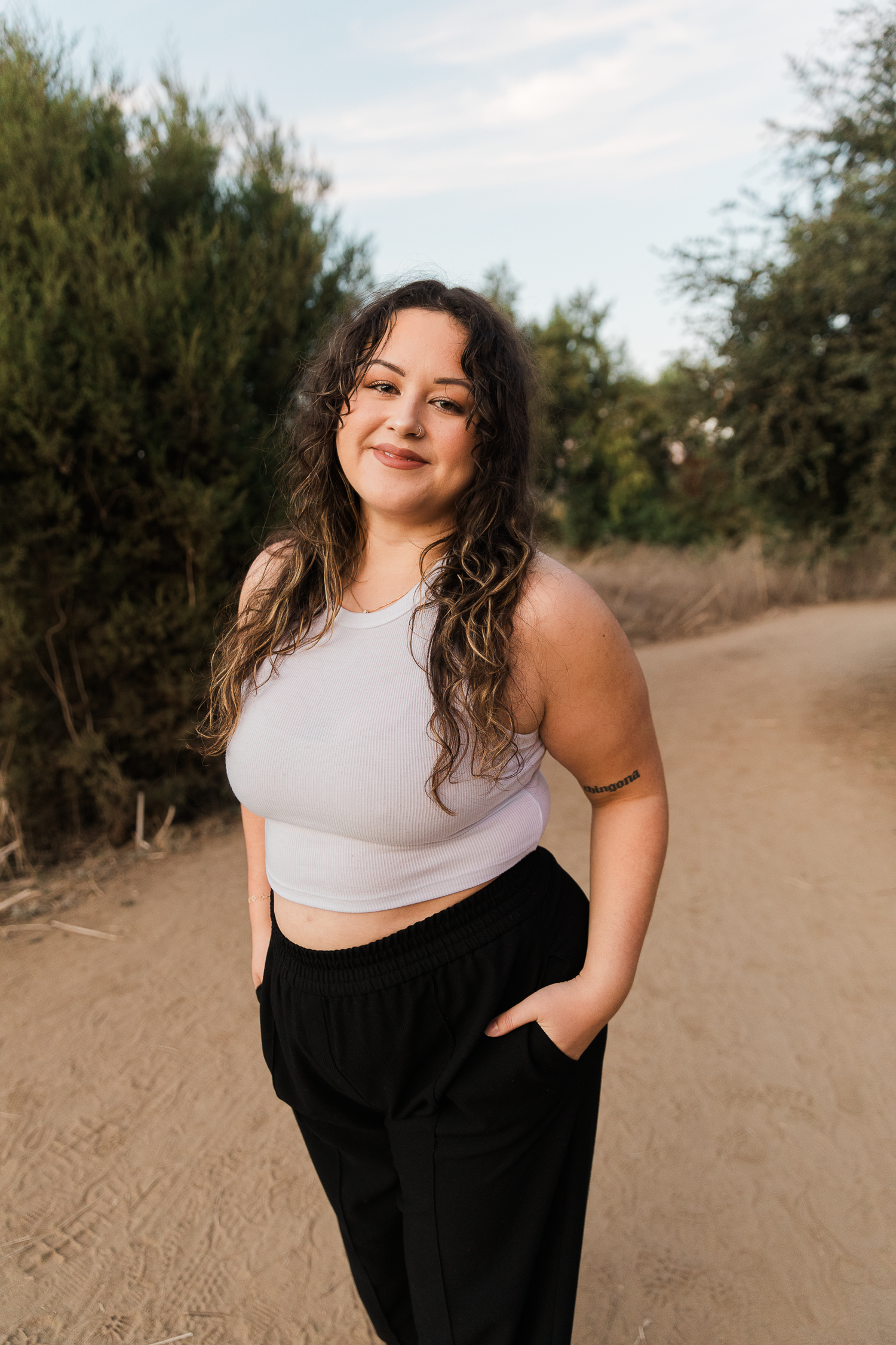 Portrait of person in crop top and black pants on dirt path with natural scenery.