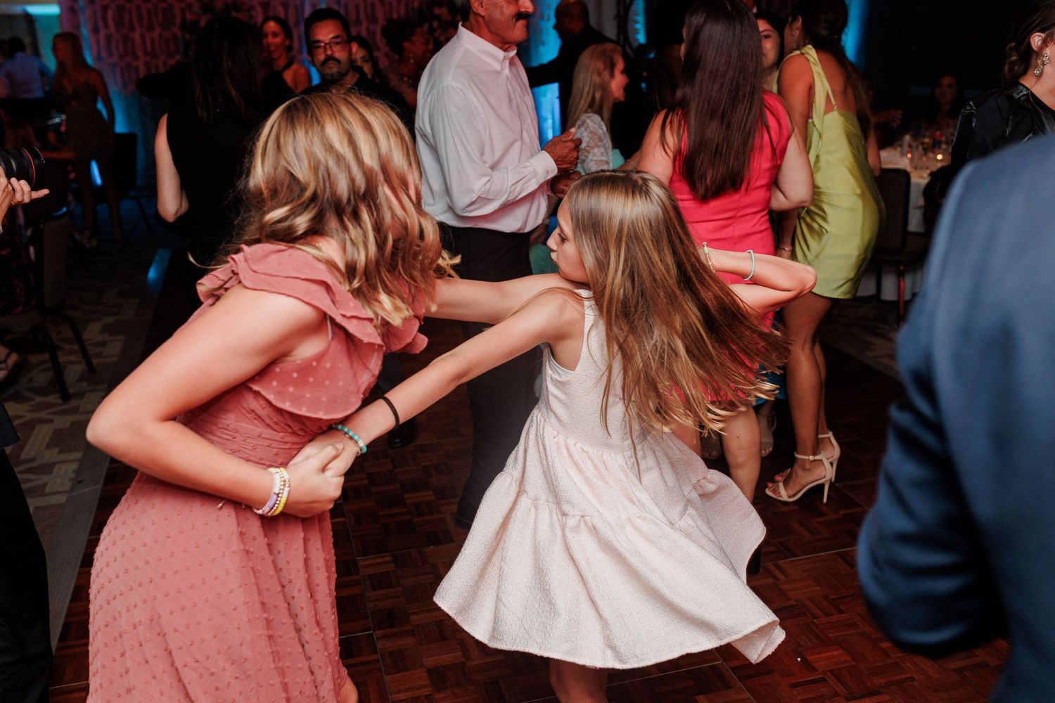 Two young girls in pink and white dresses dancing together at a wedding reception.