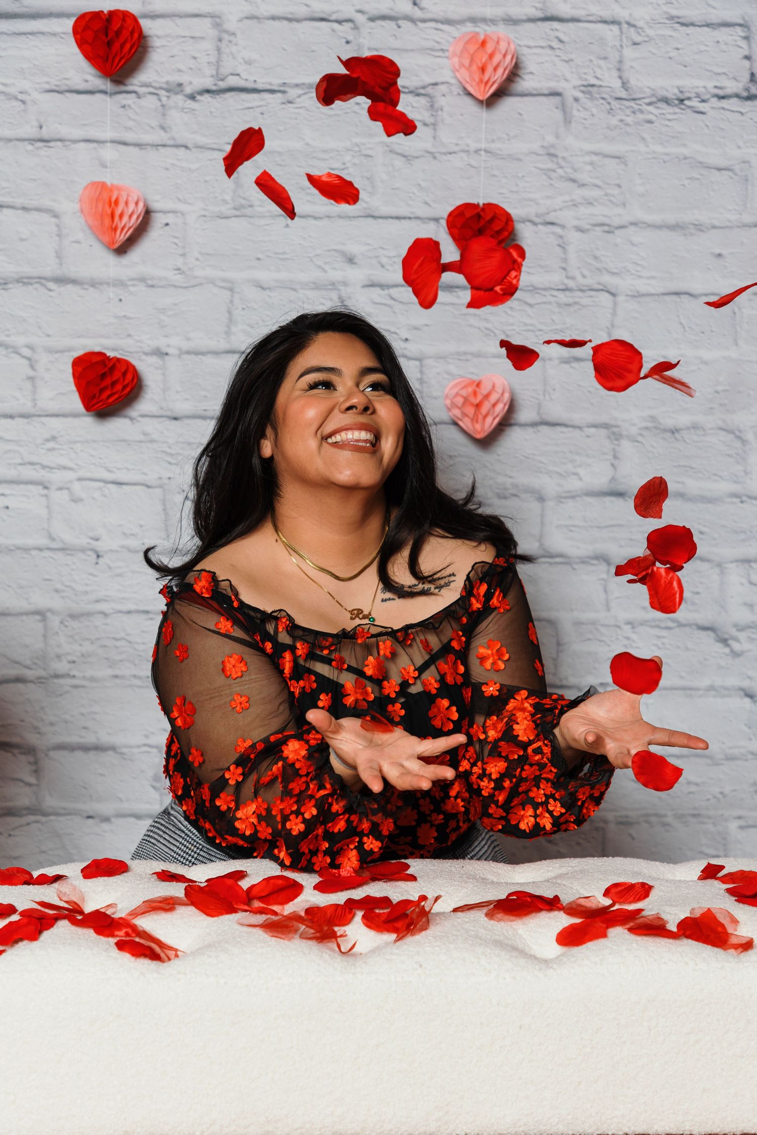 Valentine's themed portrait with red rose petals against white brick wall.