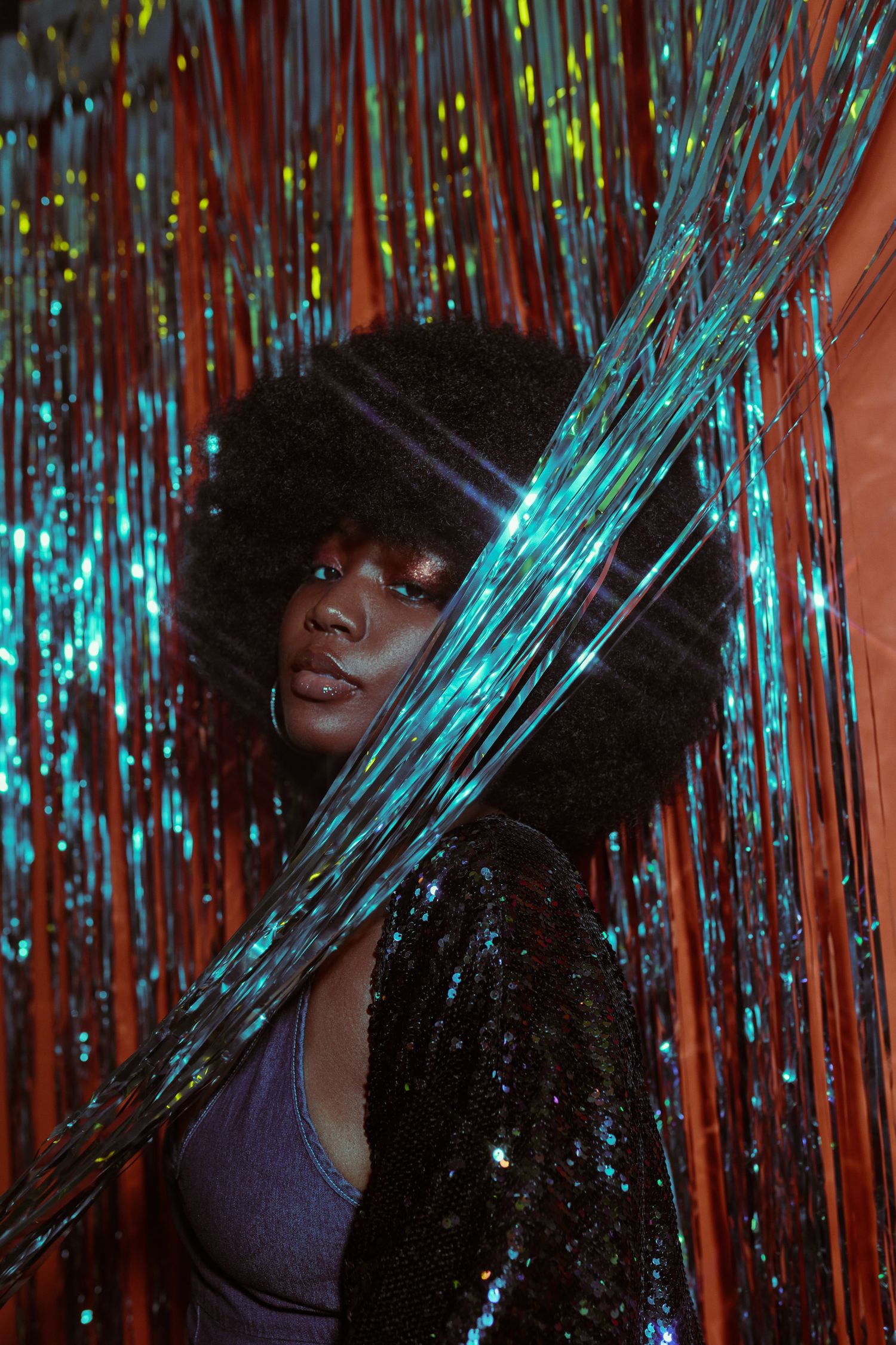 Artistic portrait through iridescent tinsel with dramatic lighting effects.