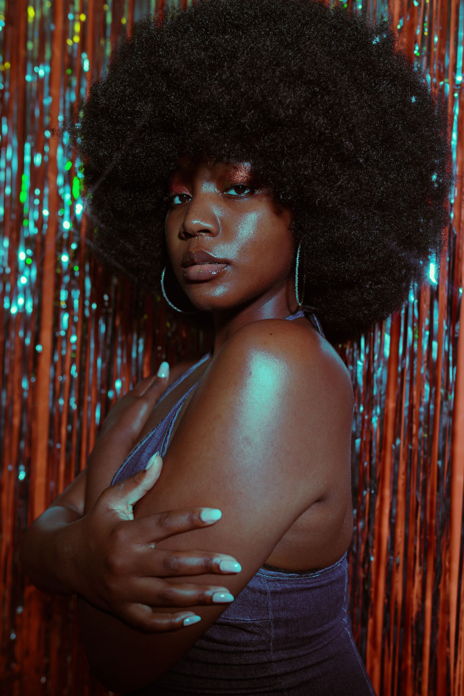 Moody portrait with teal lighting against metallic tinsel backdrop.