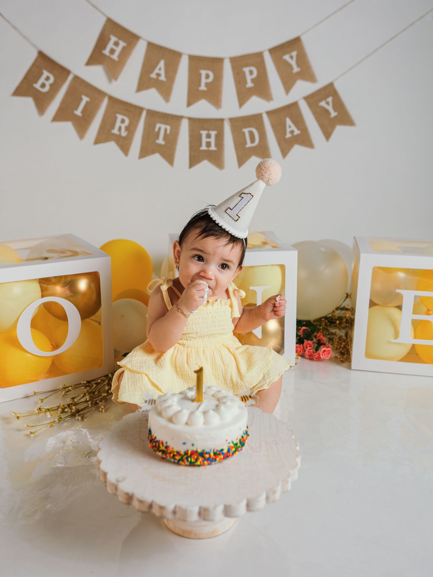 Birthday party setup with white cake, yellow balloons, and kraft paper banner.