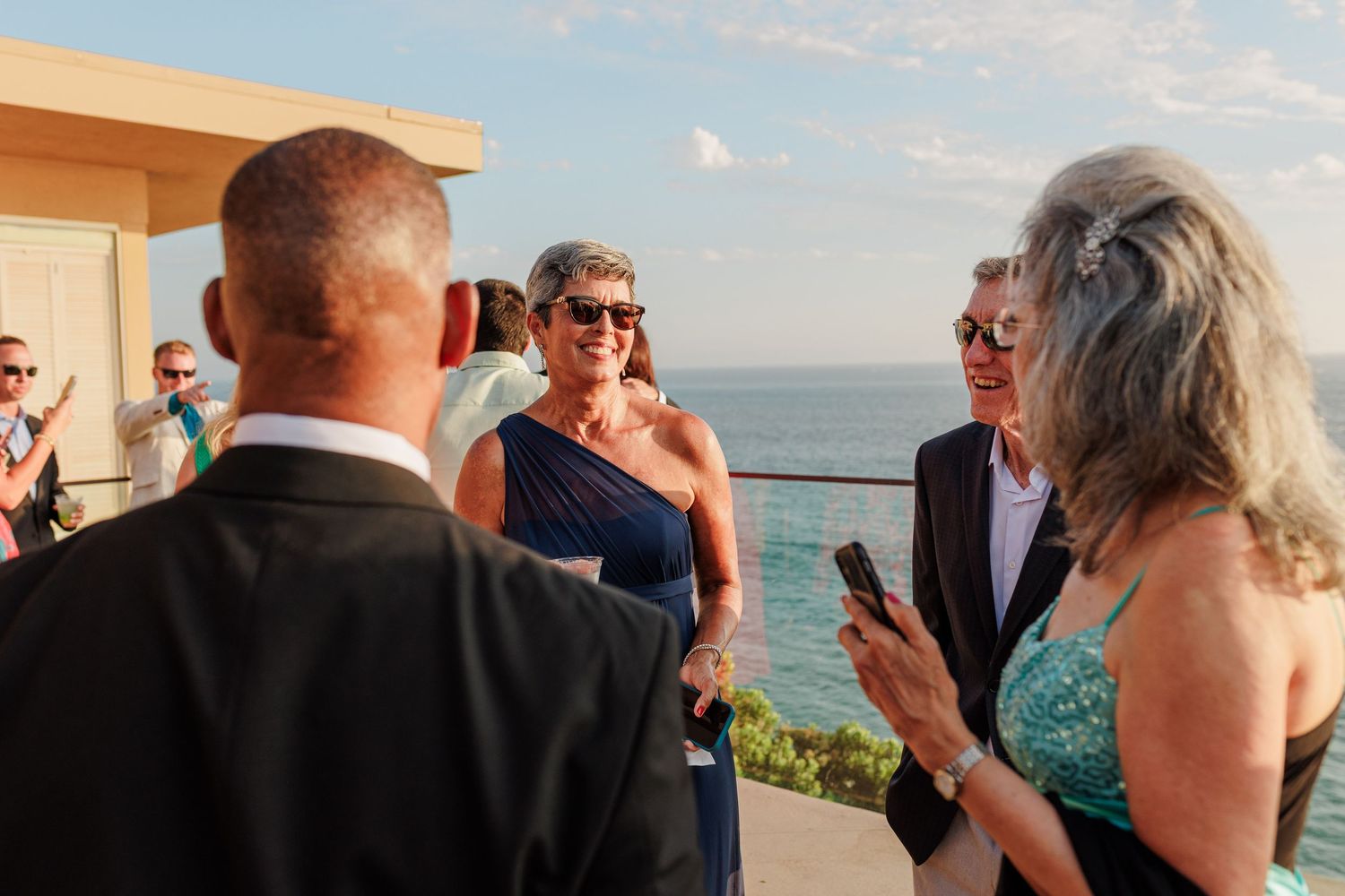 Guests socializing at an outdoor wedding reception with ocean views on a sunny day.