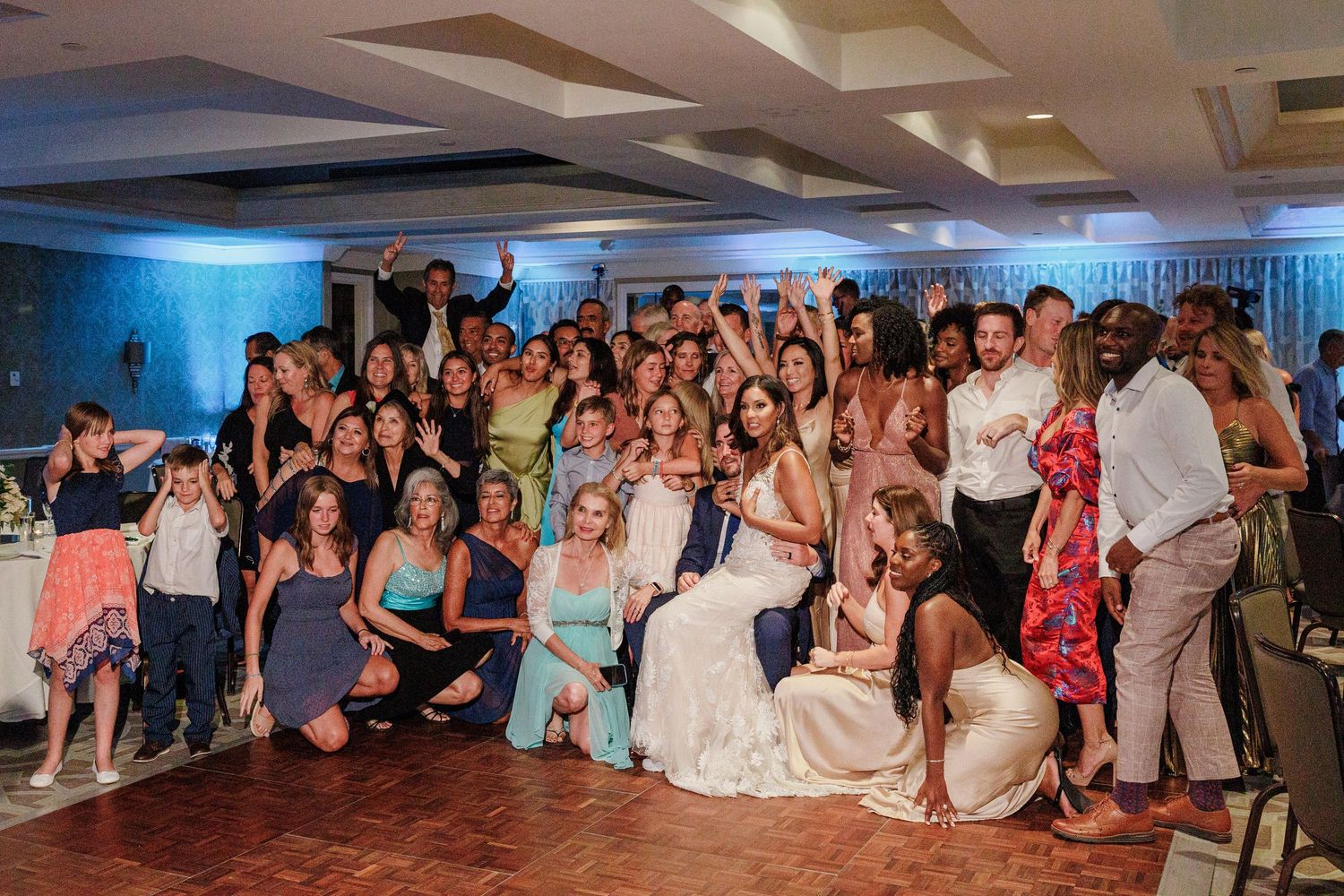 Large group of wedding guests pose with bride and groom on the dance floor.