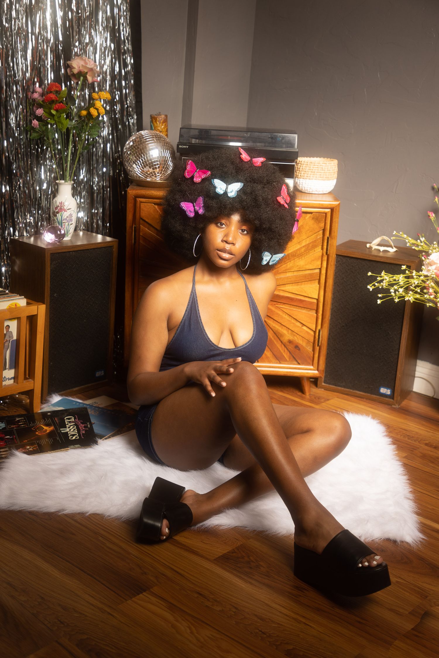 Retro-styled photo with a rattan chair, wooden floor, and silver tinsel backdrop creating a vintage aesthetic.