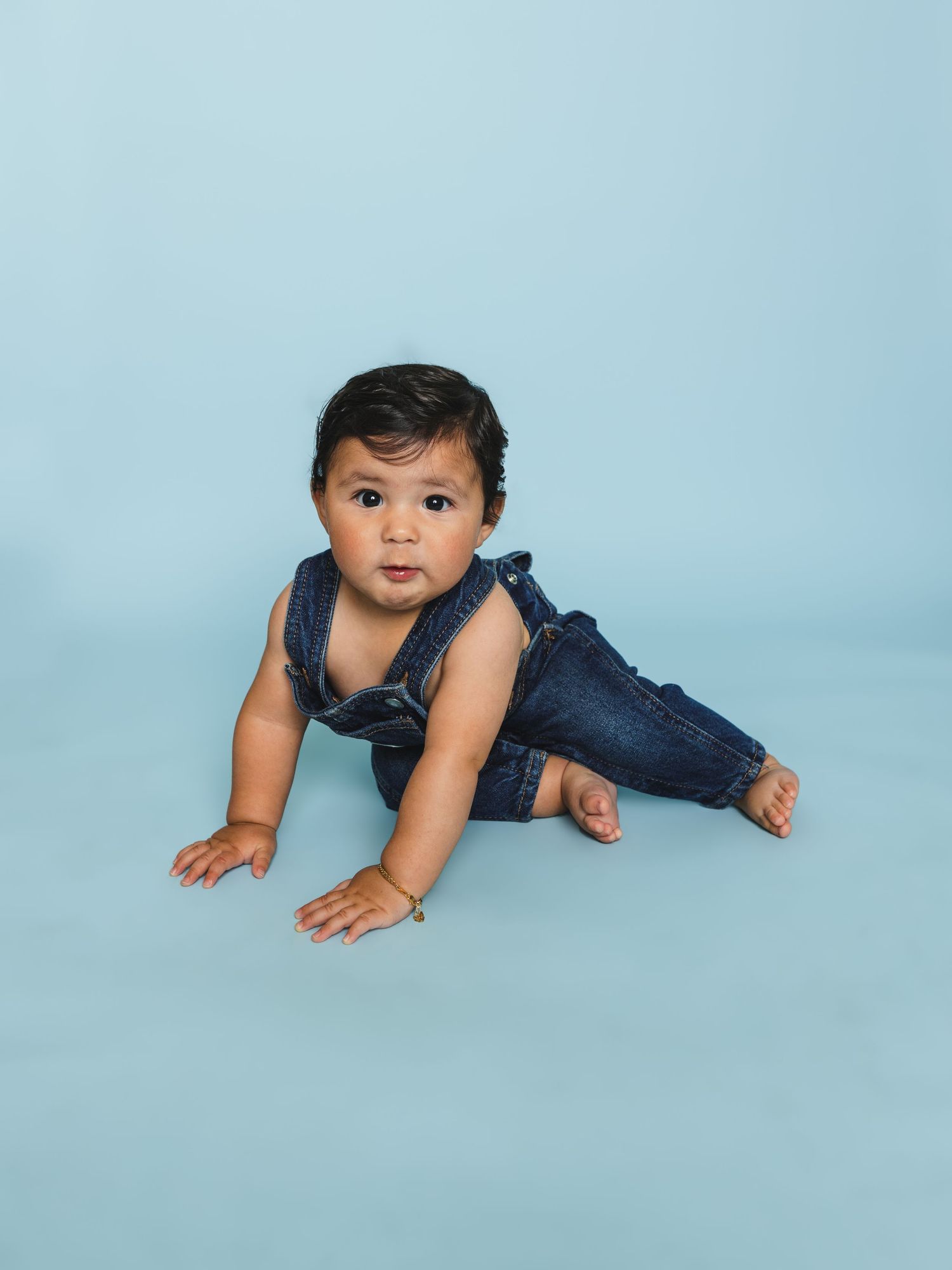 Baby in denim overalls crawling and smiling during professional photo session.