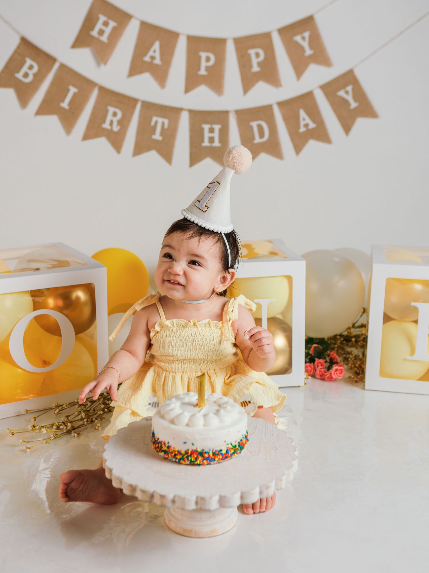 First birthday celebration with sprinkle-covered cake and festive banner decorations.