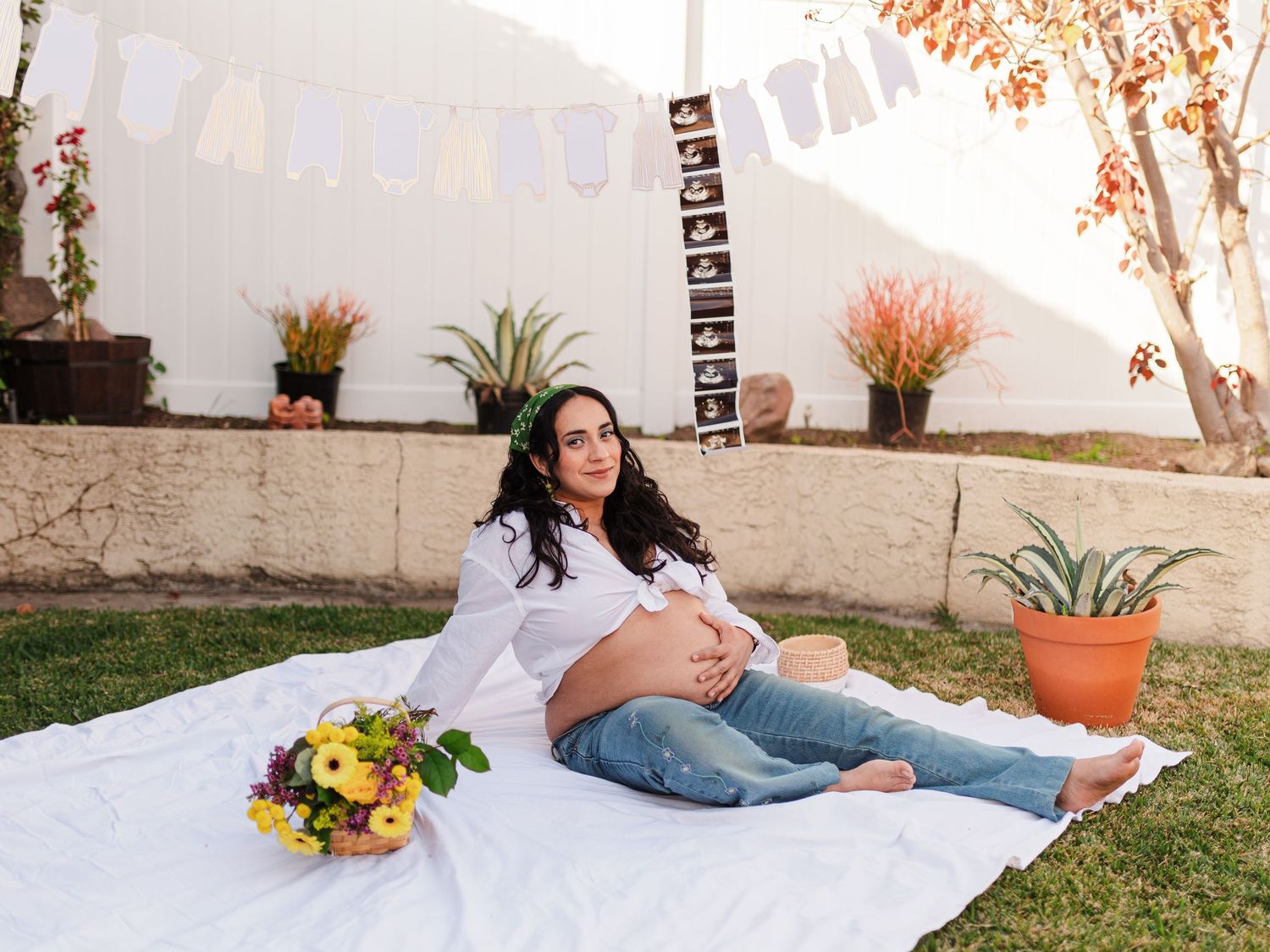 Maternity photo session in garden with white fence and floral arrangements.