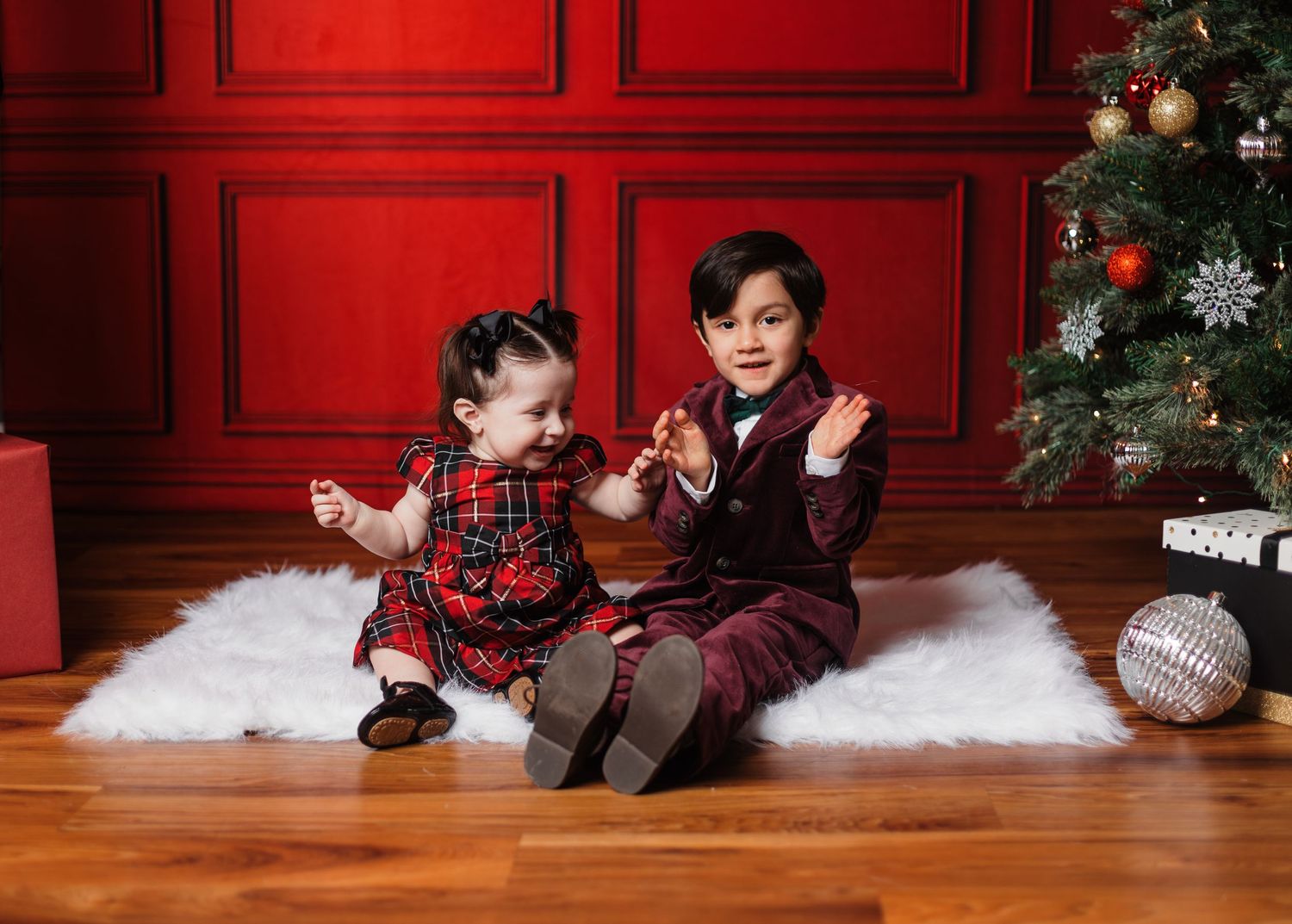 Holiday photo scene with red paneled walls, Christmas tree, and white floor decorations.