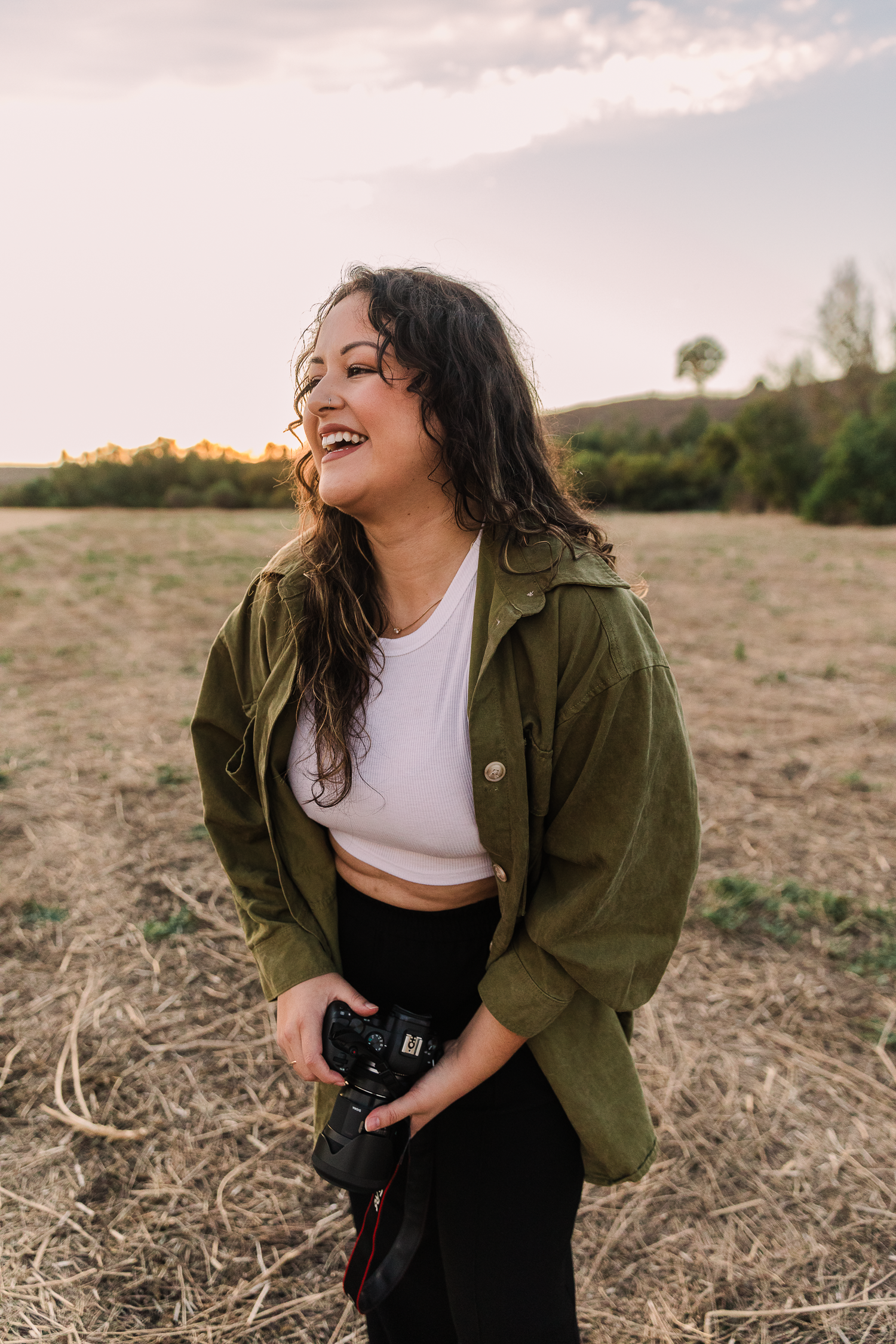 Candid portrait of person laughing in olive jacket and camera during golden hour.