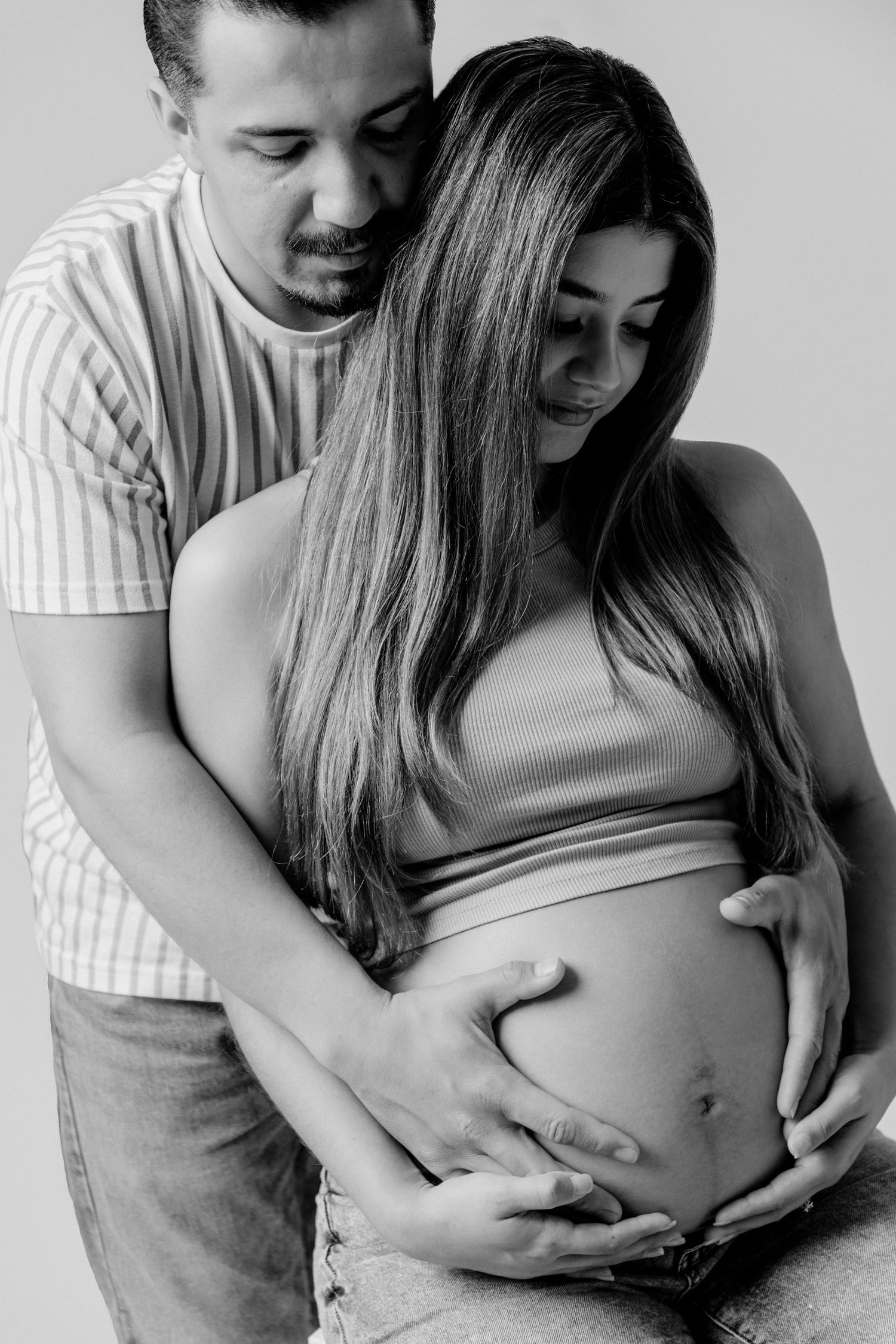 Black and white maternity photo showing tender moment as couple embraces growing baby bump.