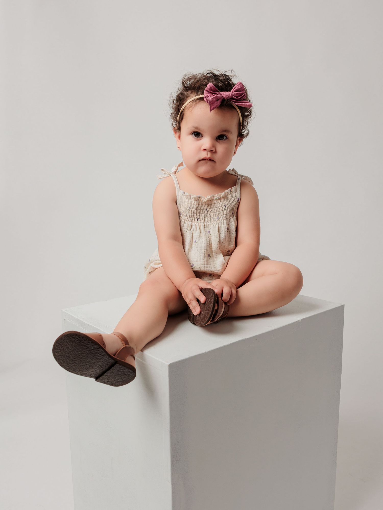 Small child in vintage dress and bow sits on white pedestal.