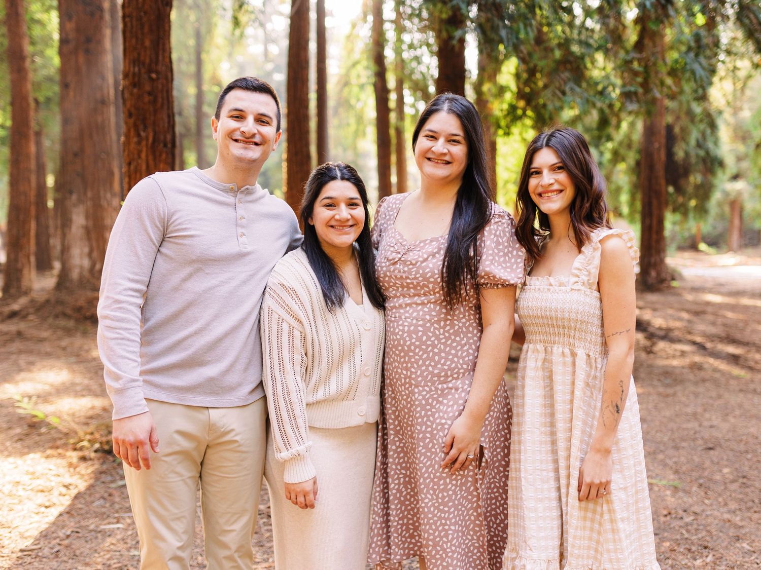 A group poses together in coordinated pink and beige outfits against a backdrop of tall trees.