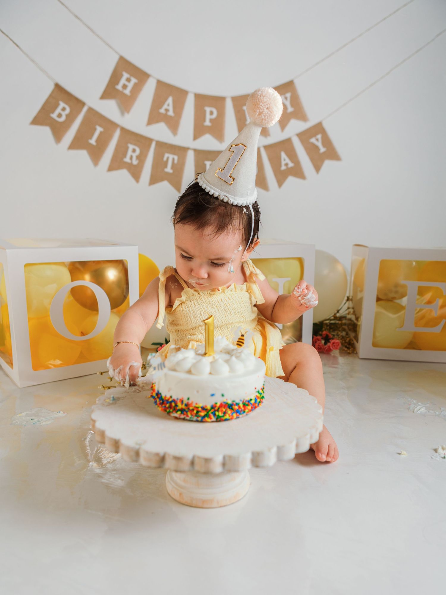 Cake smash photography setup with yellow dress and white frosted cake.