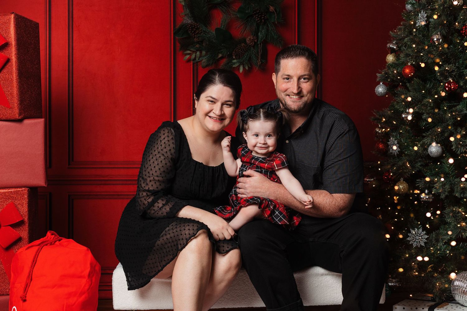 Family Christmas portrait setup with decorated tree and red wall backdrop.