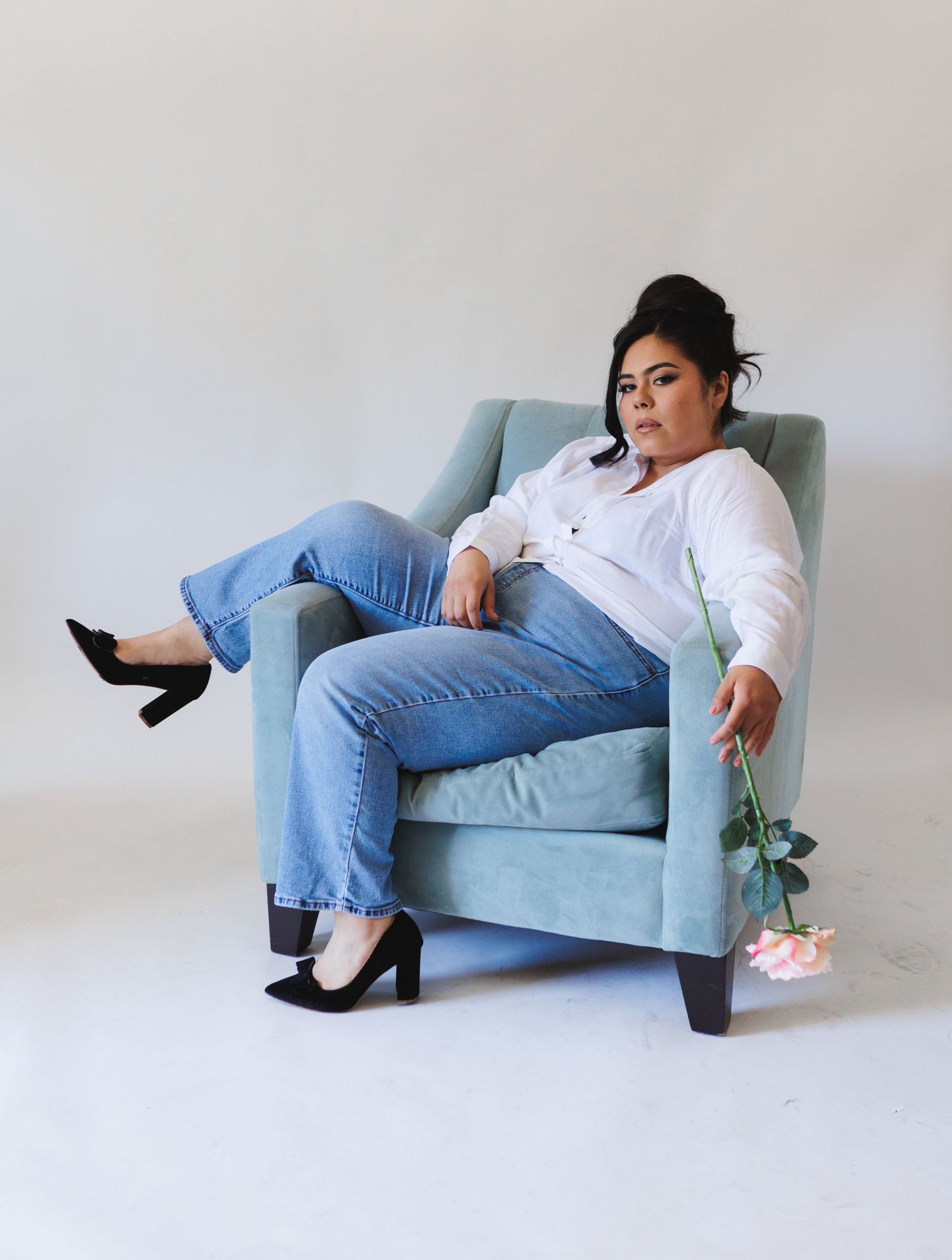 Fashion photo series on blue chaise lounge wearing white shirt, jeans and black heels.