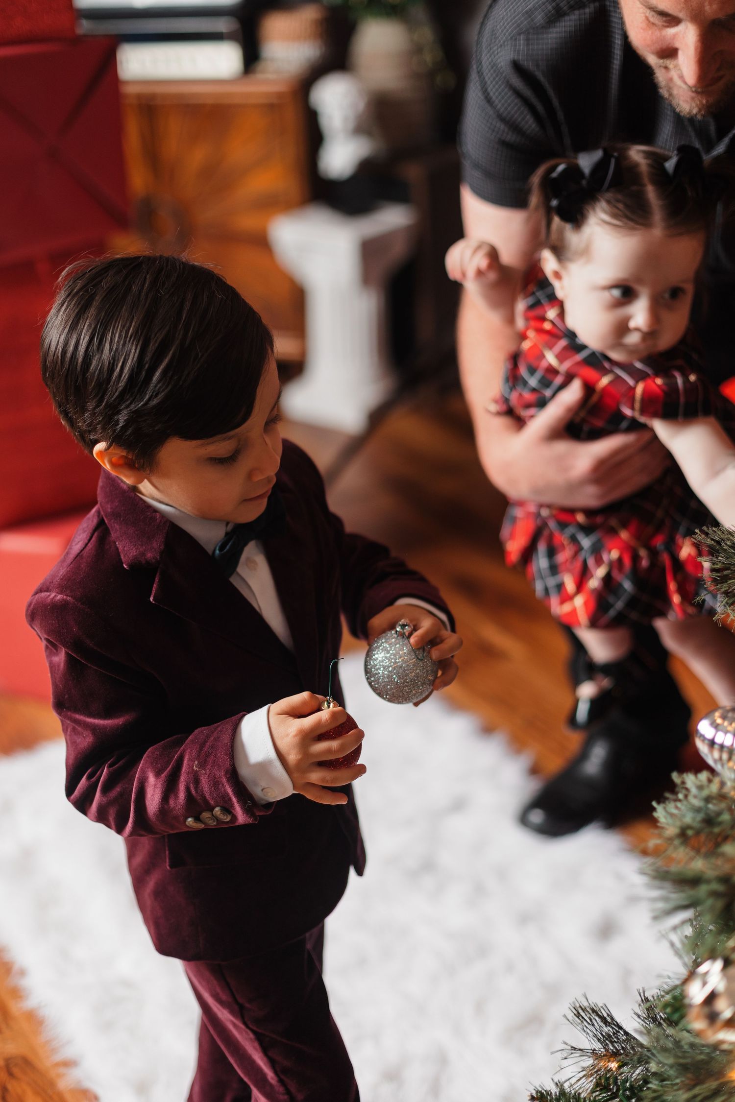 Candid holiday moments captured against Christmas tree and snowy white floor setting.