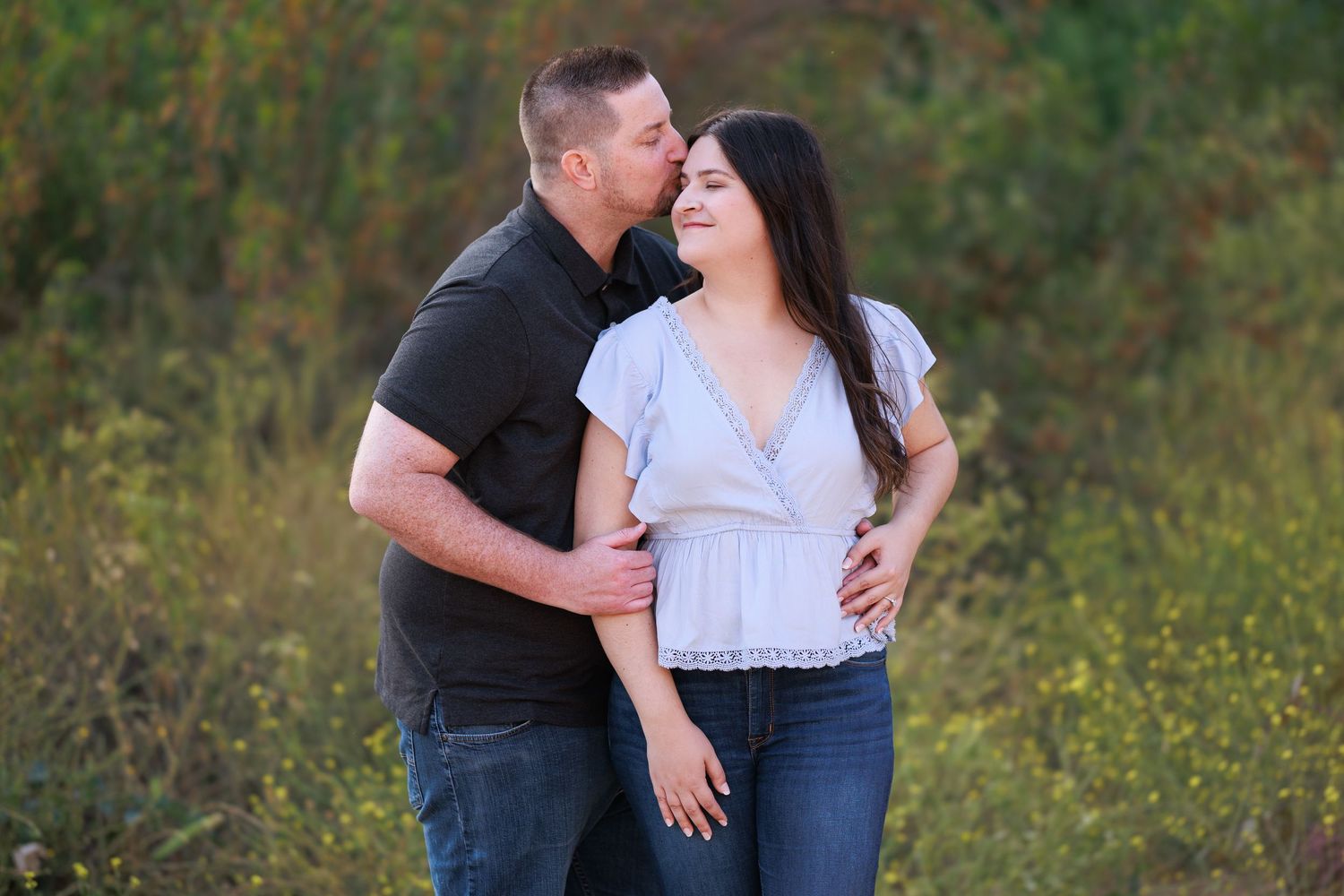 Couple embracing in outdoor field with golden wildflowers at sunset.