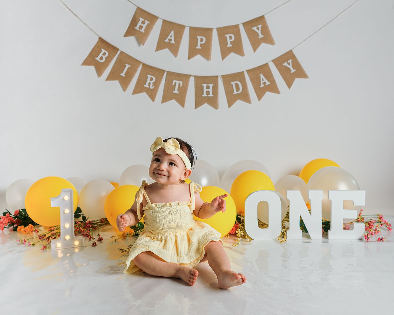 Baby's first birthday celebration setup with gold 'Happy Birthday' banner and yellow decorations.