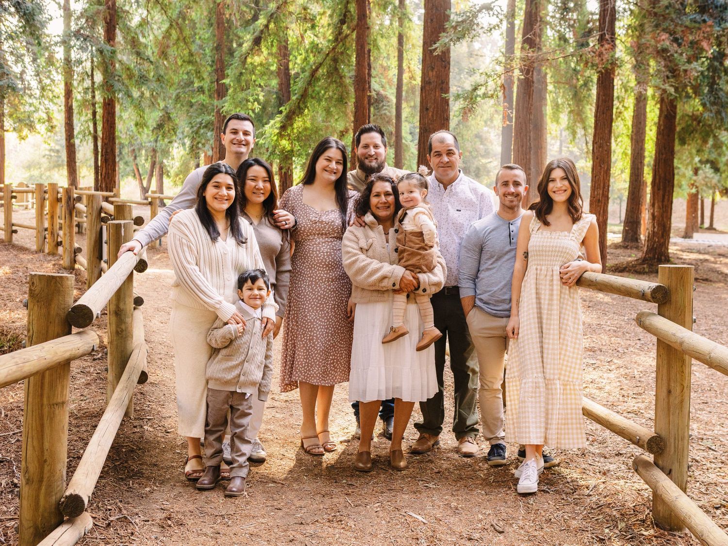 Outdoor family gathering in wooded setting wearing neutral colored clothing.