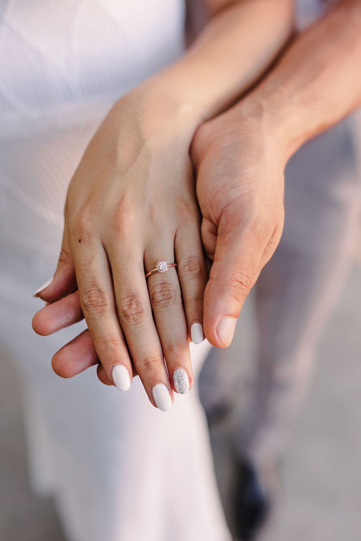 Close-up of hands showing engagement ring with soft natural lighting.