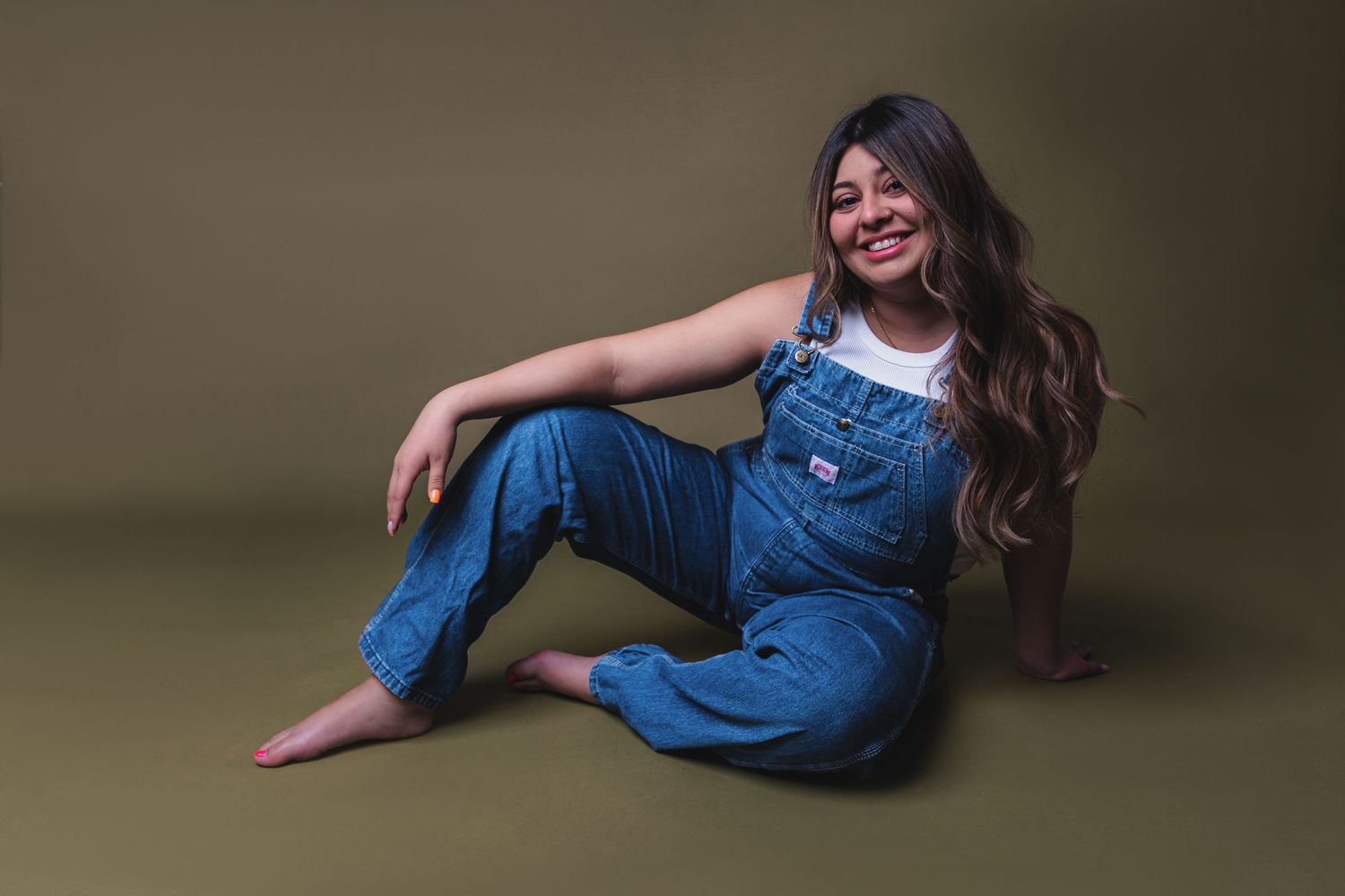 A person in jeans relaxes on a green studio backdrop during a photoshoot.