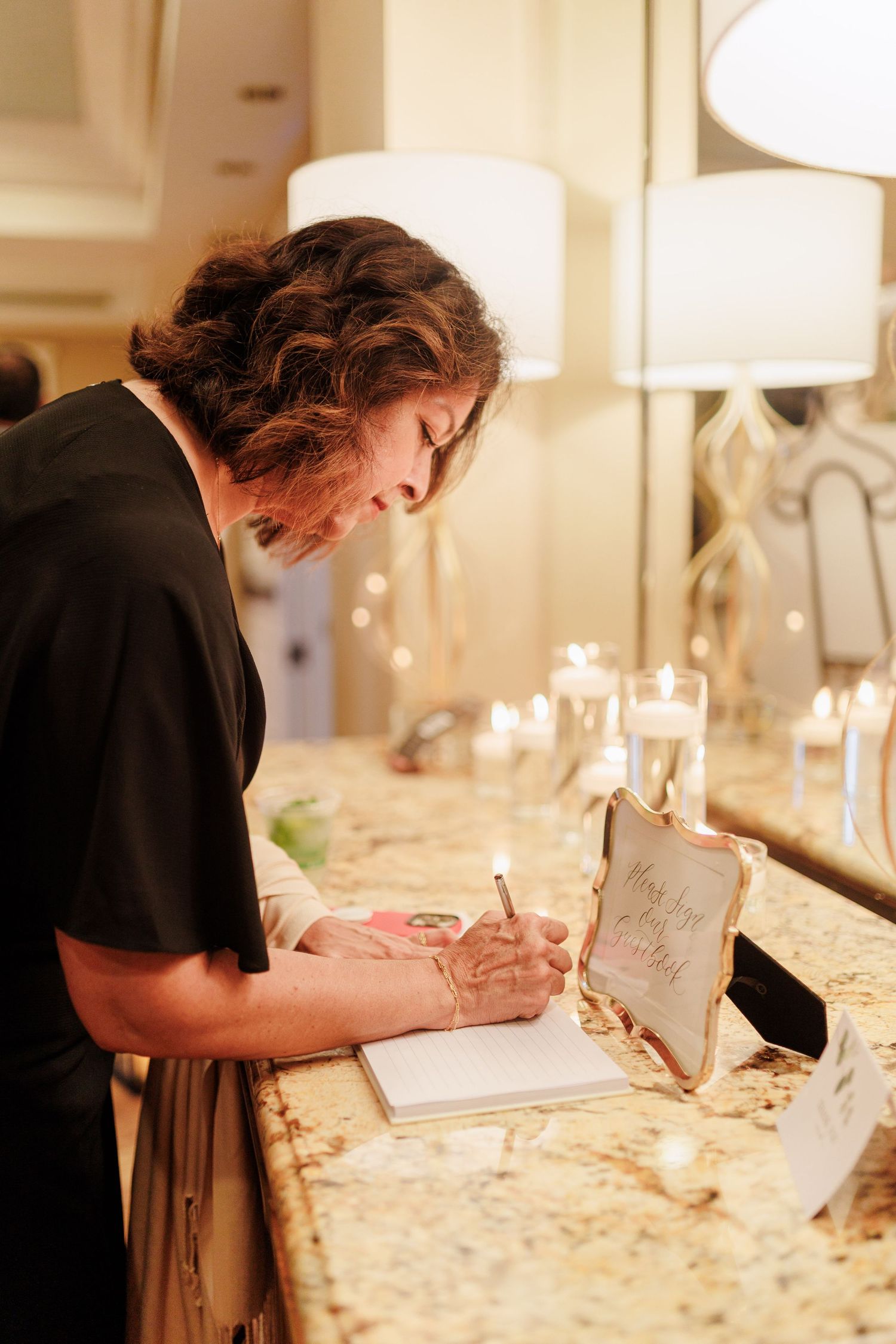 Wedding guest signing the guestbook at a warmly lit reception table with candles and decorative frame.