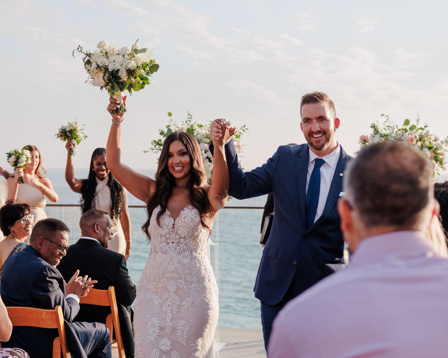 Joyful newlyweds celebrating recessional at outdoor waterfront wedding ceremony with guests.
