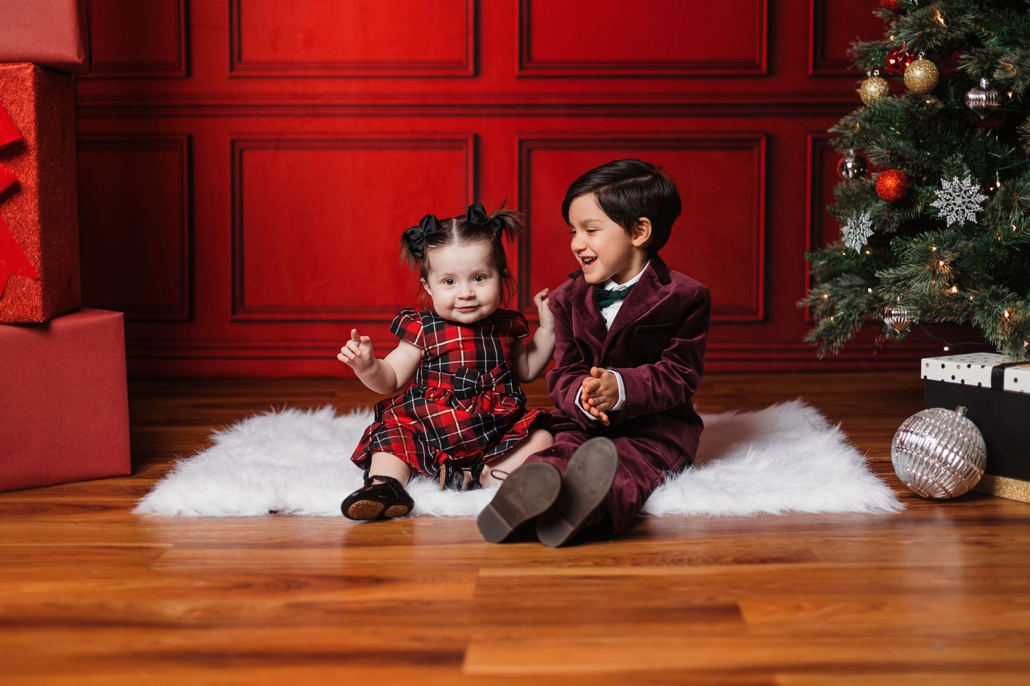 Christmas photo setup with red walls, decorated tree, and white faux fur floor covering.
